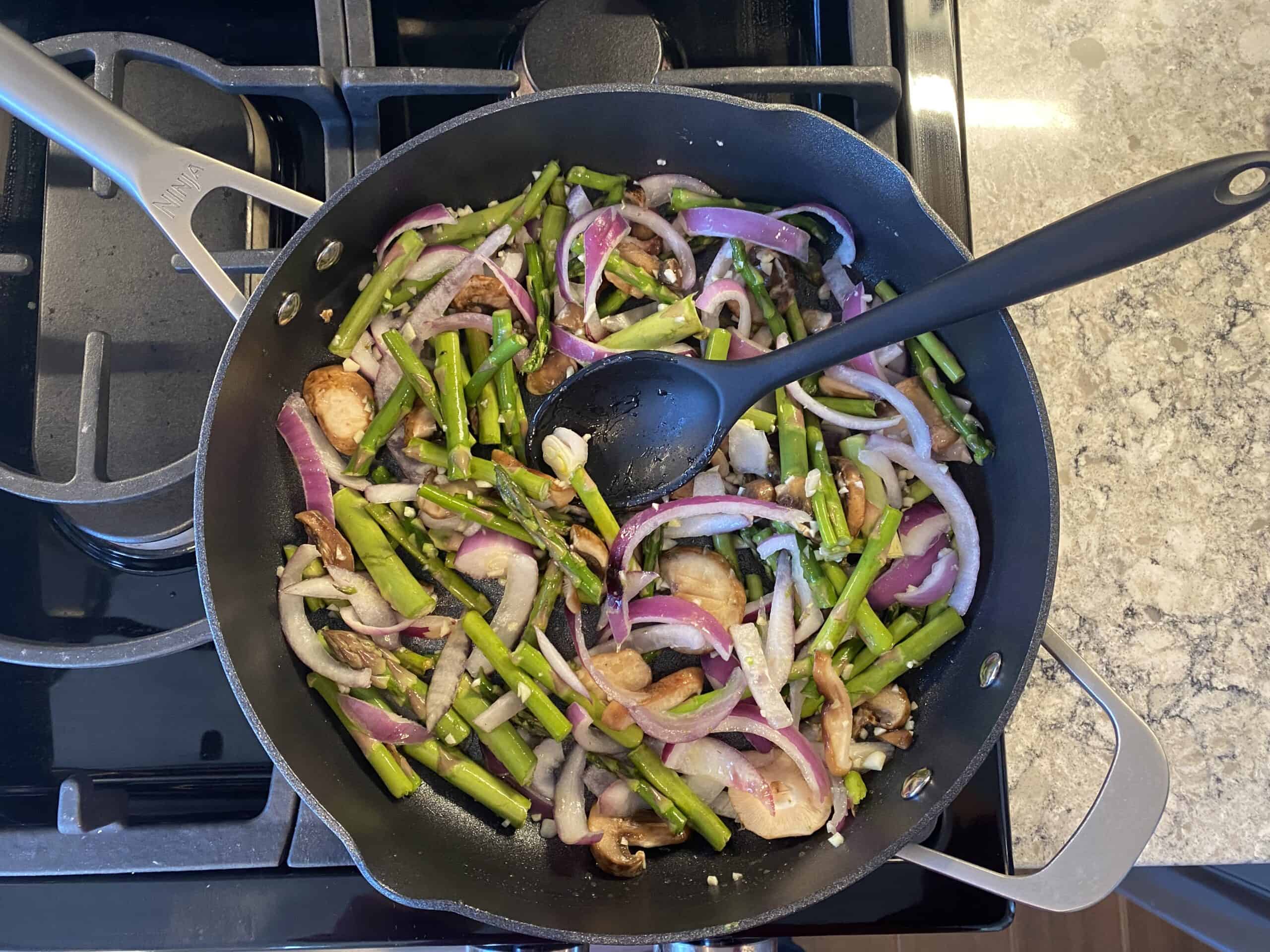 Mushrooms, asparagus, onions, and garlic sauteing in a pan.