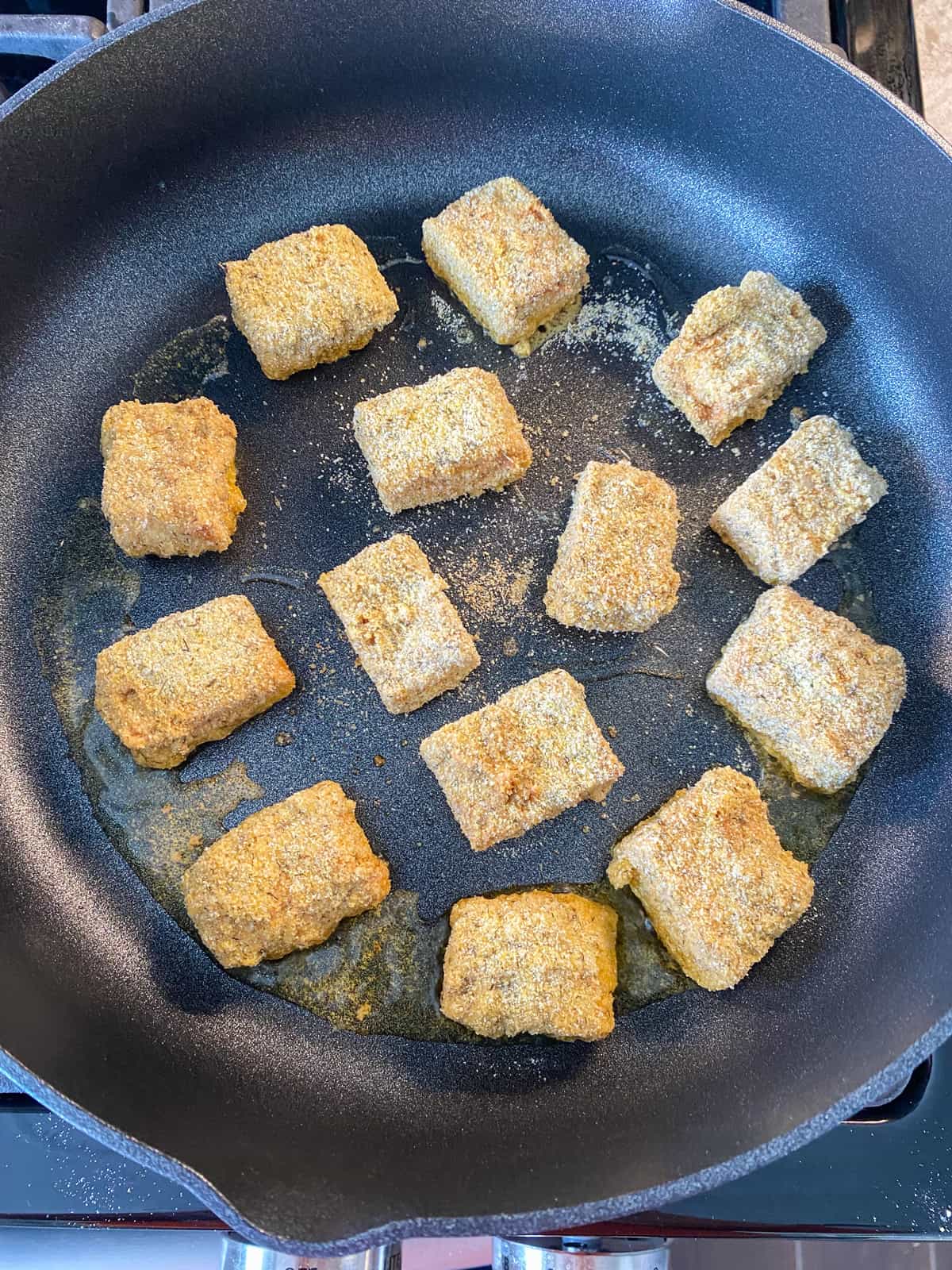 Tempeh coated with cornmeal breading, cooking in a skillet.