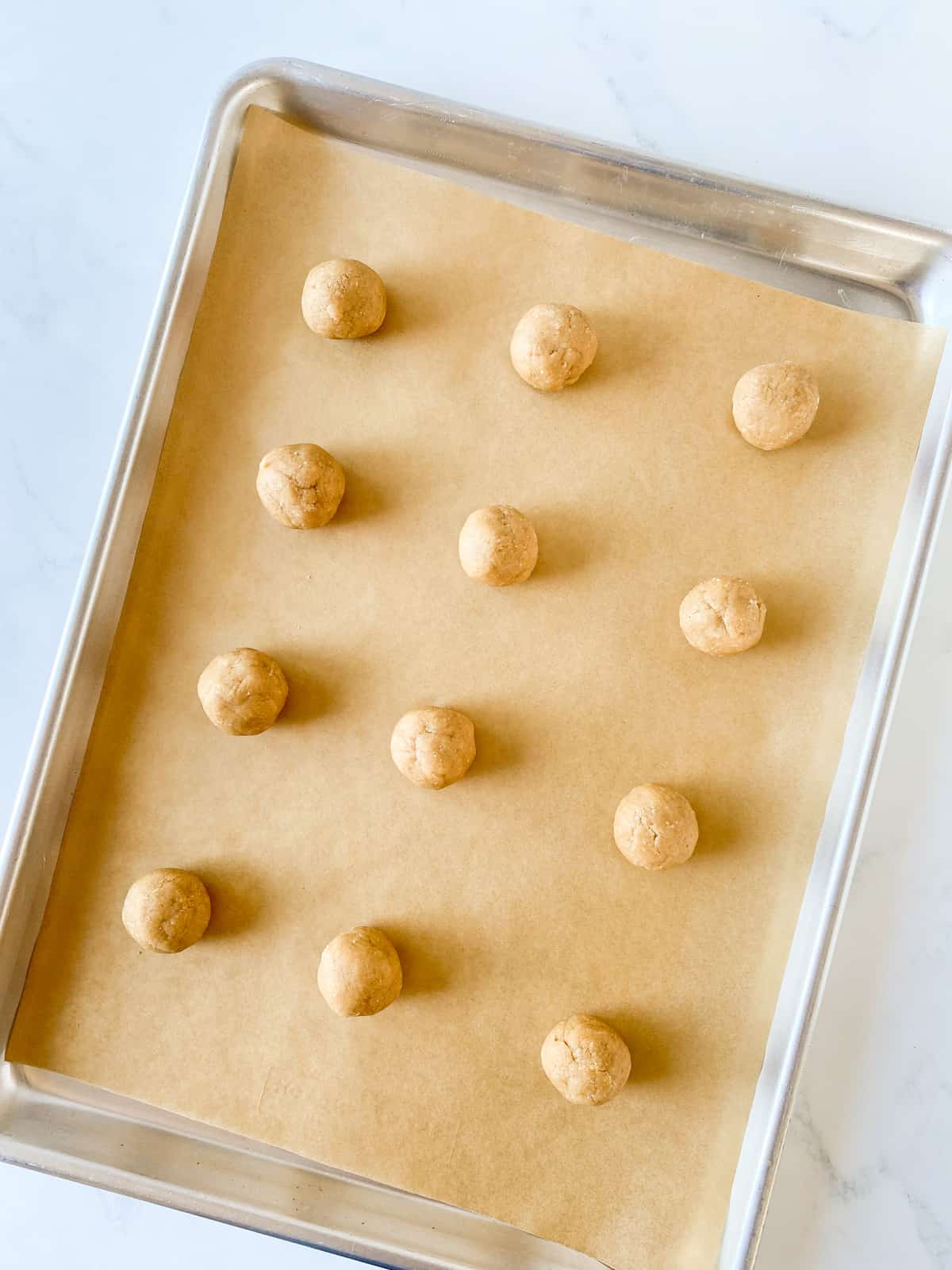 Cookie dough formed into balls on a cookie sheet.