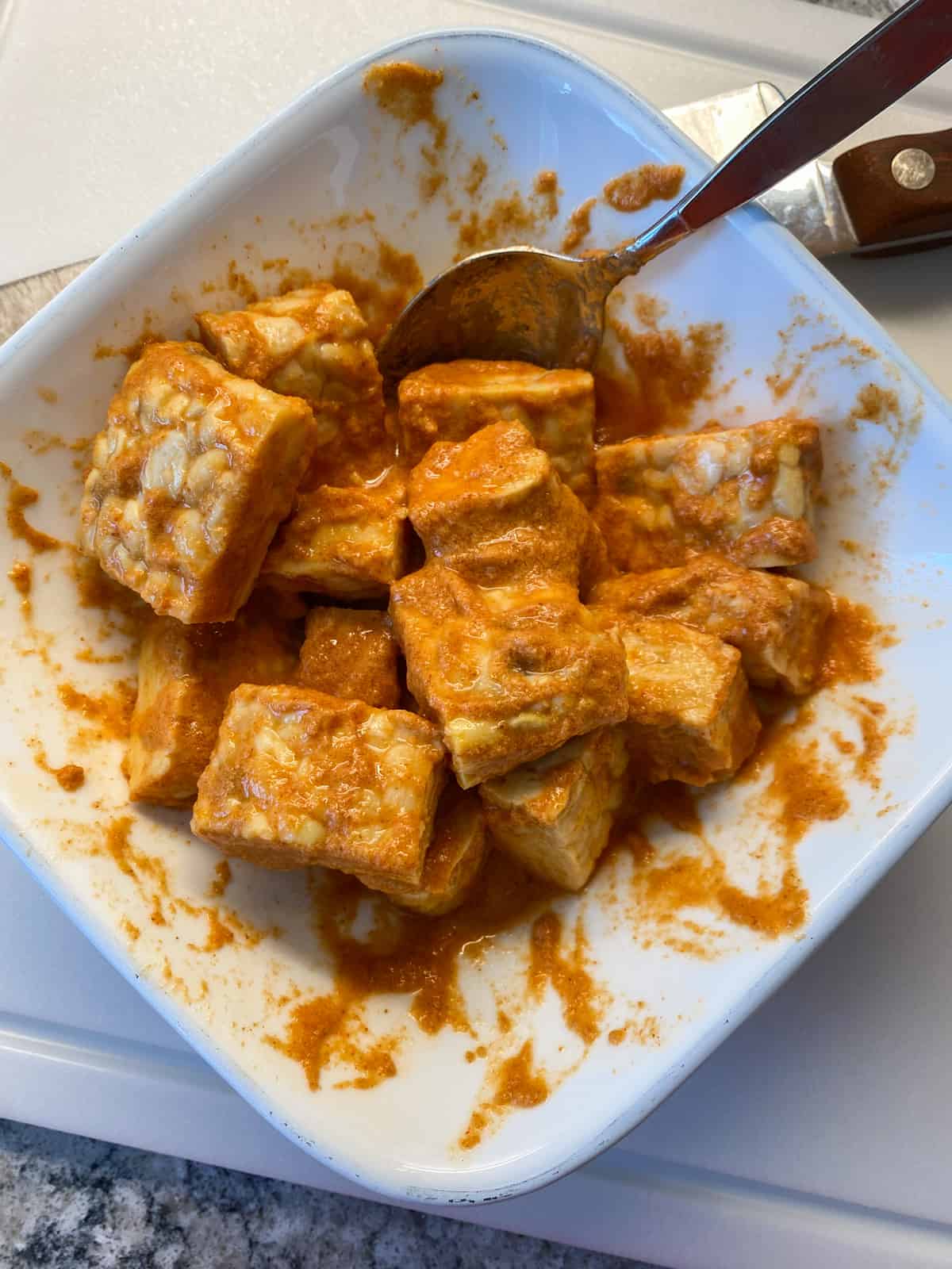 Cut up squares of tempeh mixed into Buffalo sauce to marinate.