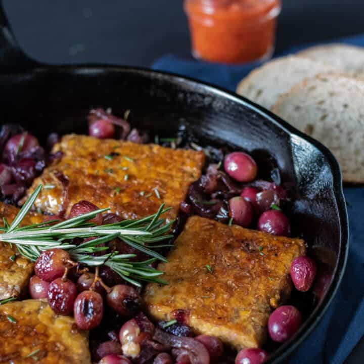 Cast iron skillet with tempeh, caramelized onions, and grapes in it. Garnished with fresh rosemary.
