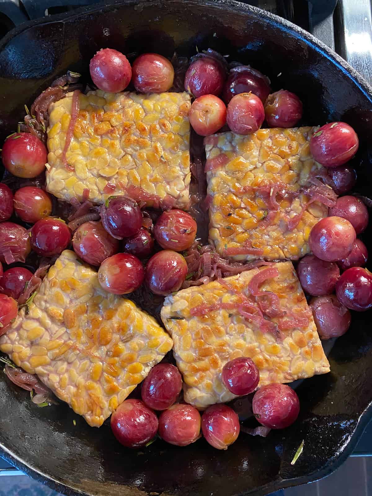 Tempeh in a skillet, with grapes and caramelized onions, ready to go in the oven.
