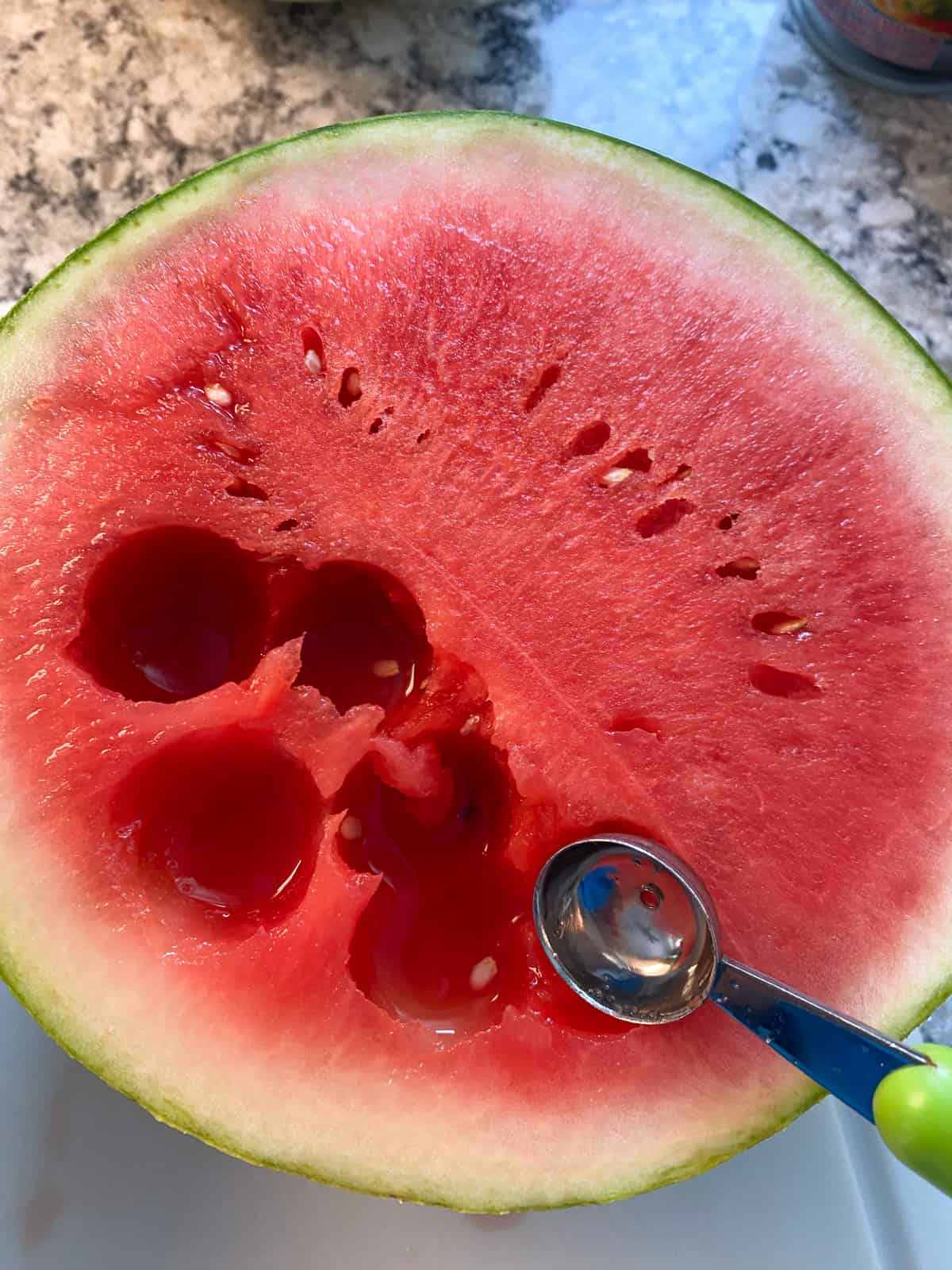 Half of a watermelon, with a melon baller, and several scoops taken from the melon.