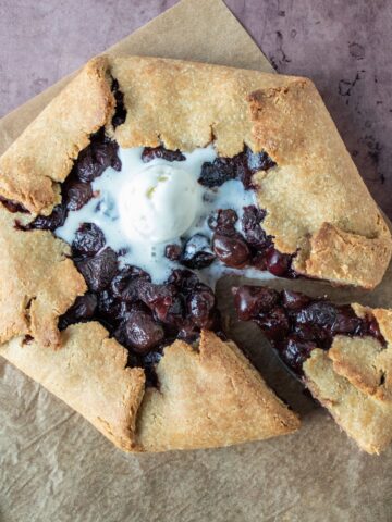 Overhead shot of cherry galette with melted ice cream on top, and a serving utensil removing a slice.