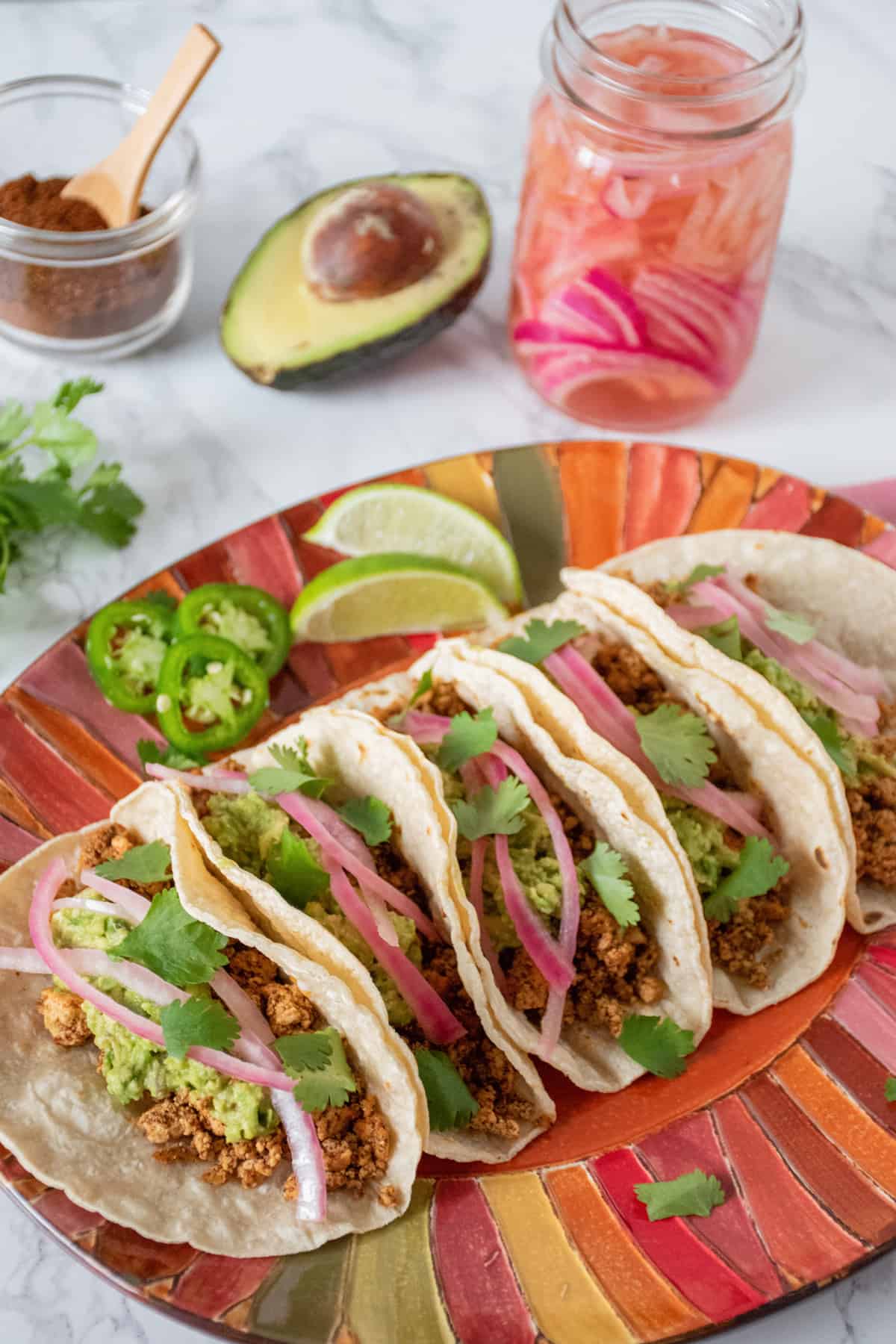 Plate of five tacos in a row, surrounded by taco fixings