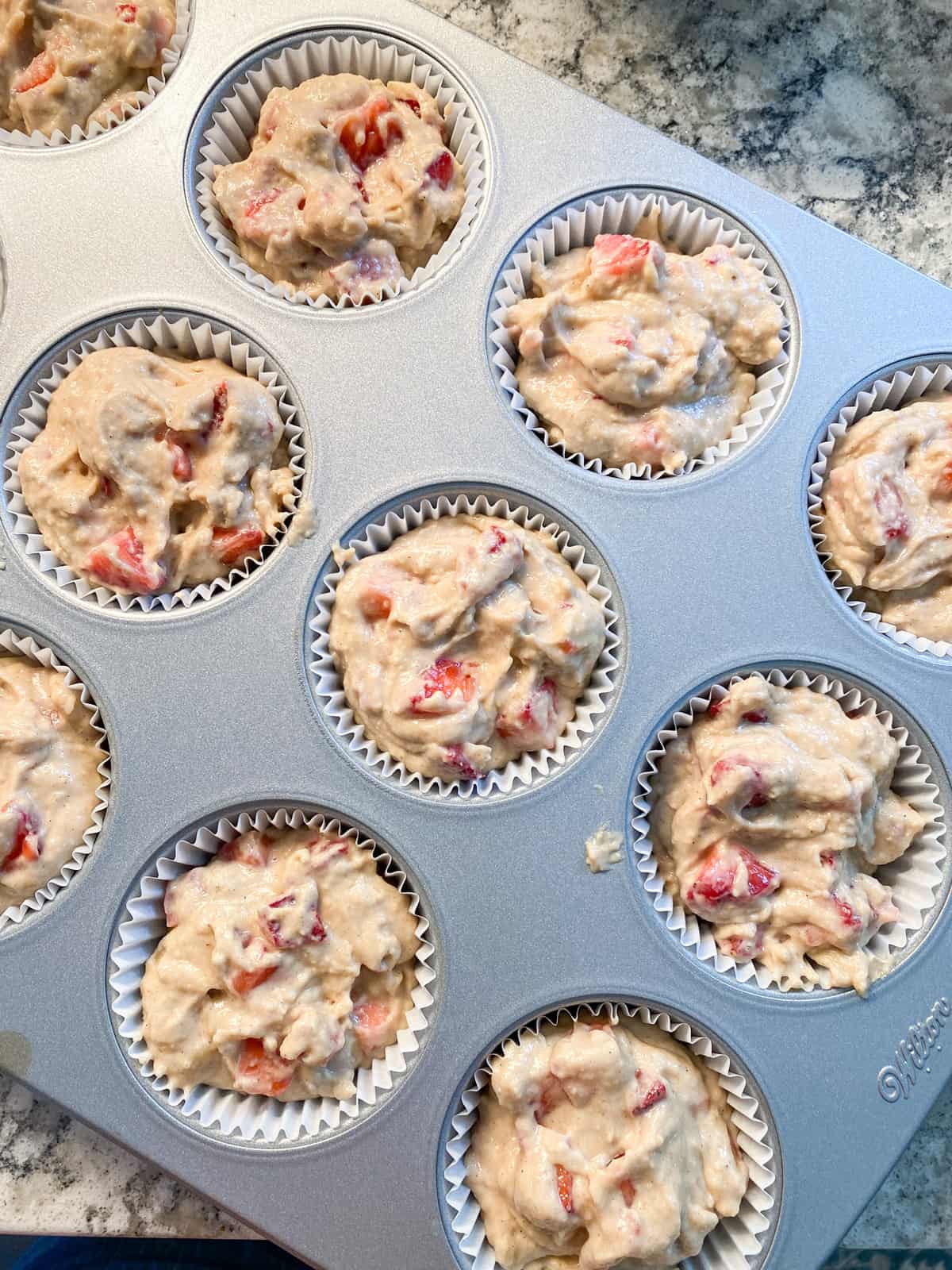 Muffin batter scooped into lined muffin pan.