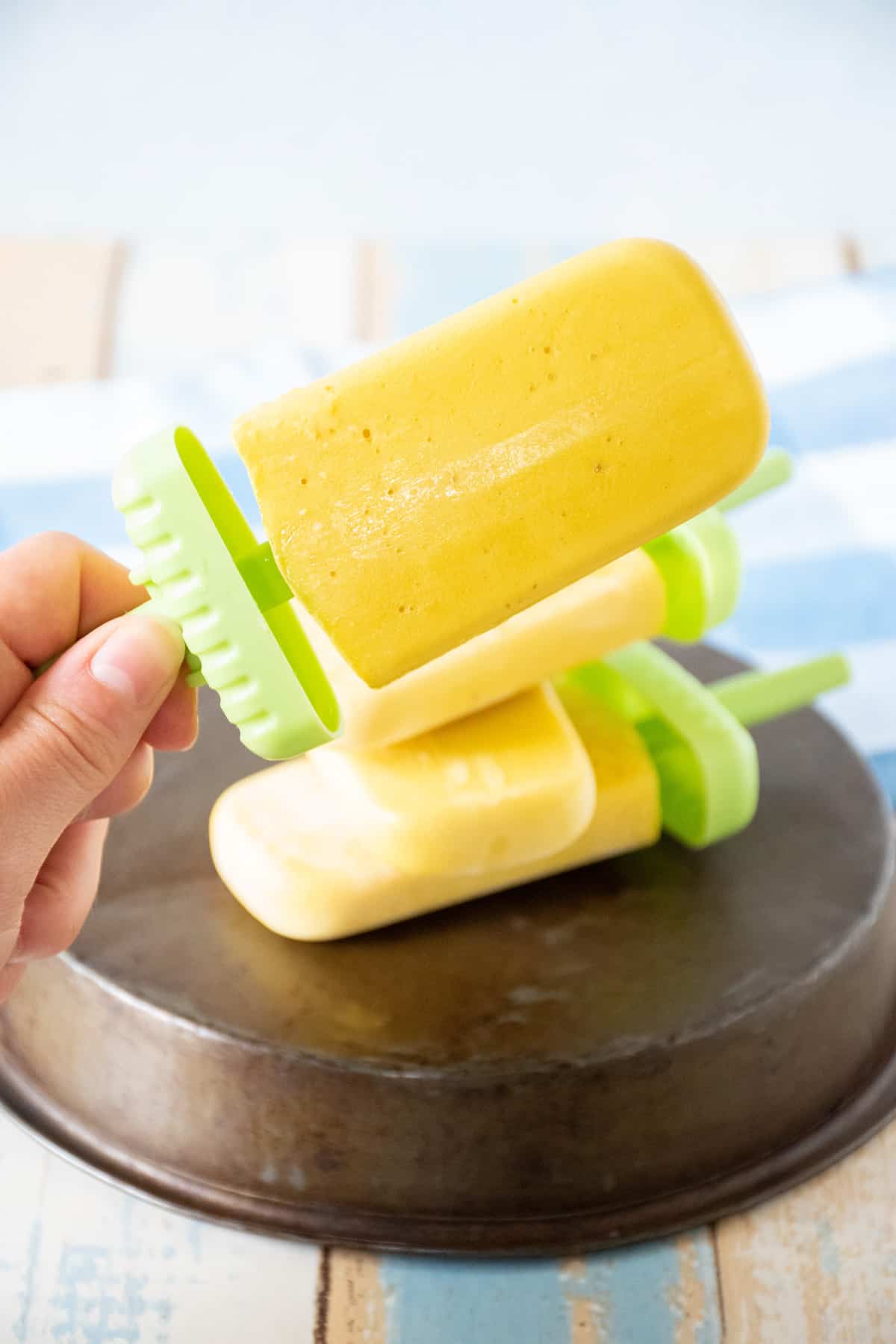 Hand holding up a popsicle, with several more popsicles lying on a dish in the background.