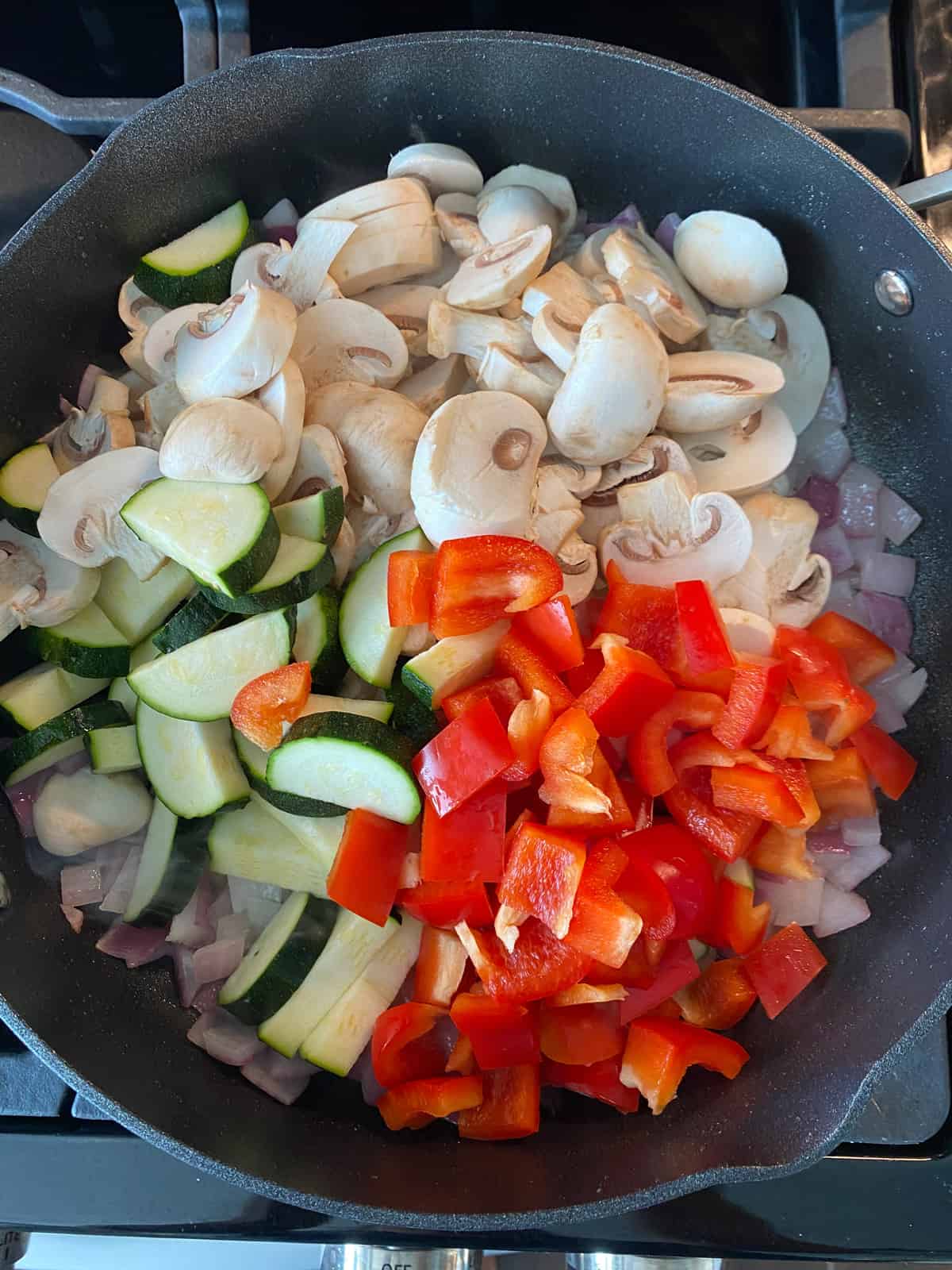Chopped vegetables added to sauteed onions, in a pan.