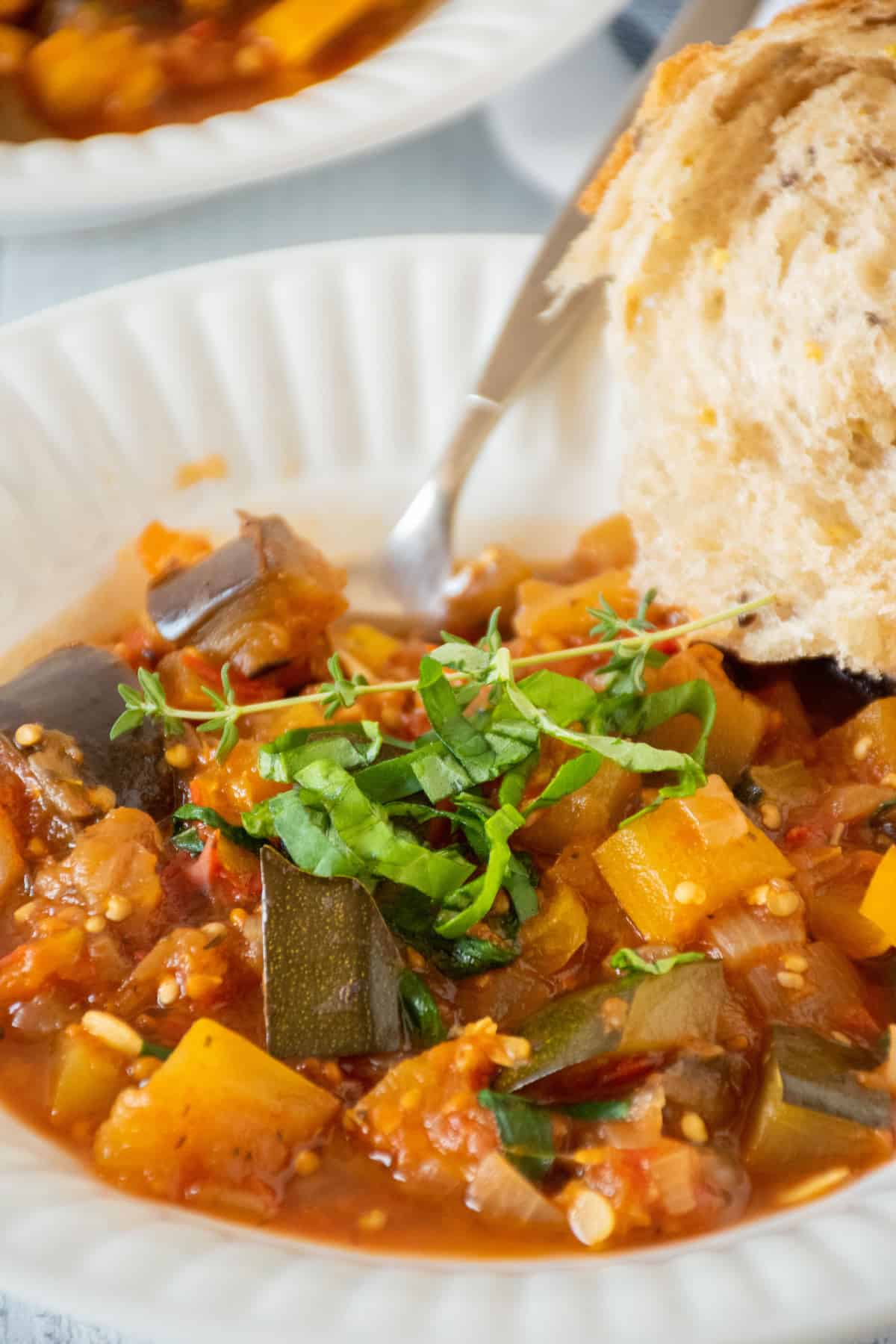 Bowl of ratatouille, with a piece of crusty bread on the side.