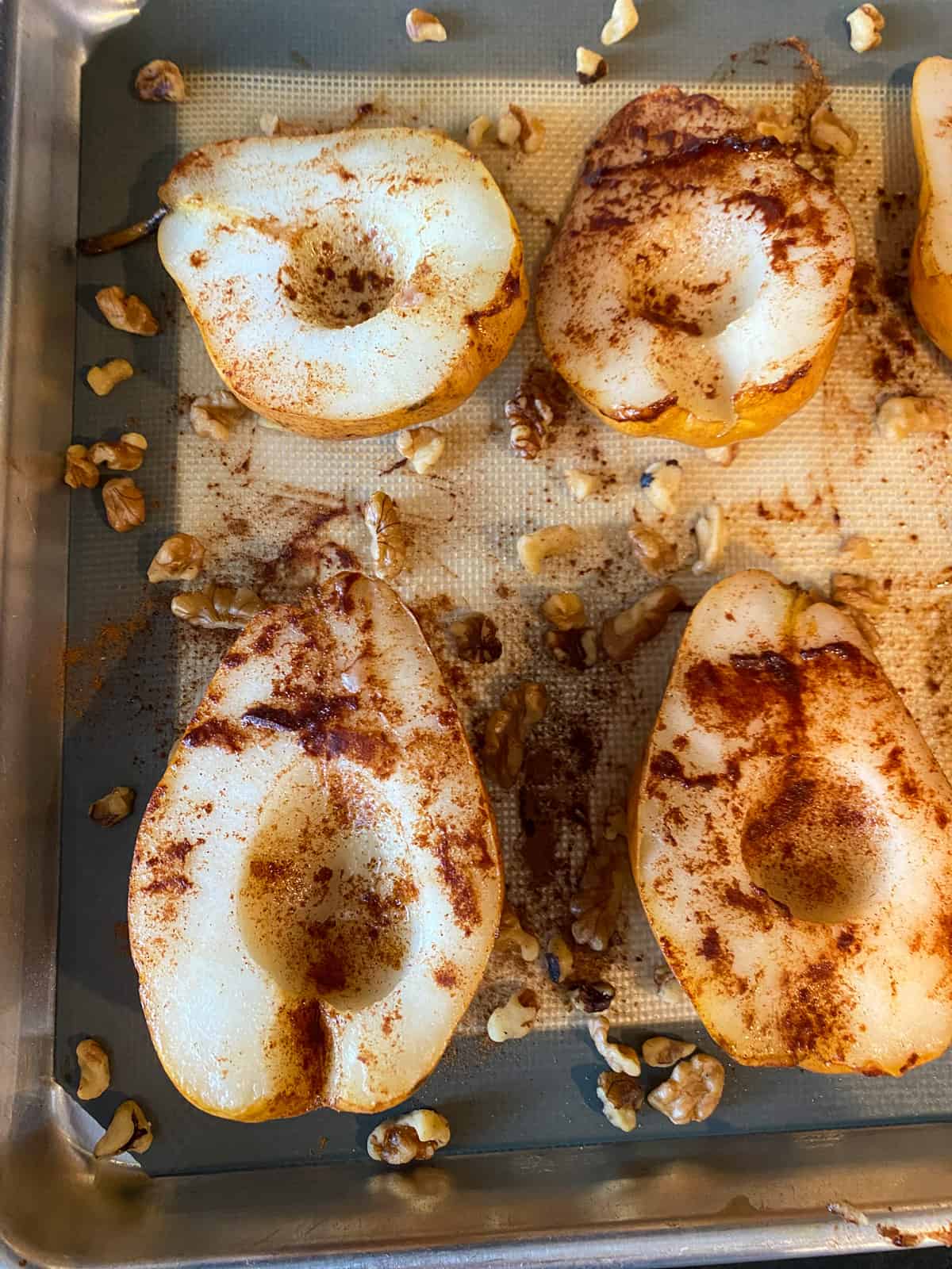 Halved pears on baking sheet, with walnuts sprinkled around them.