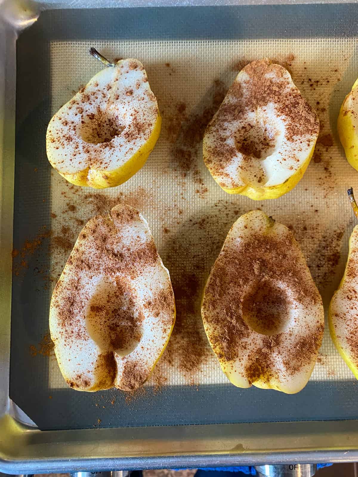 Halved pears, on a baking sheet, sprinkled with cinnamon before going into the oven.