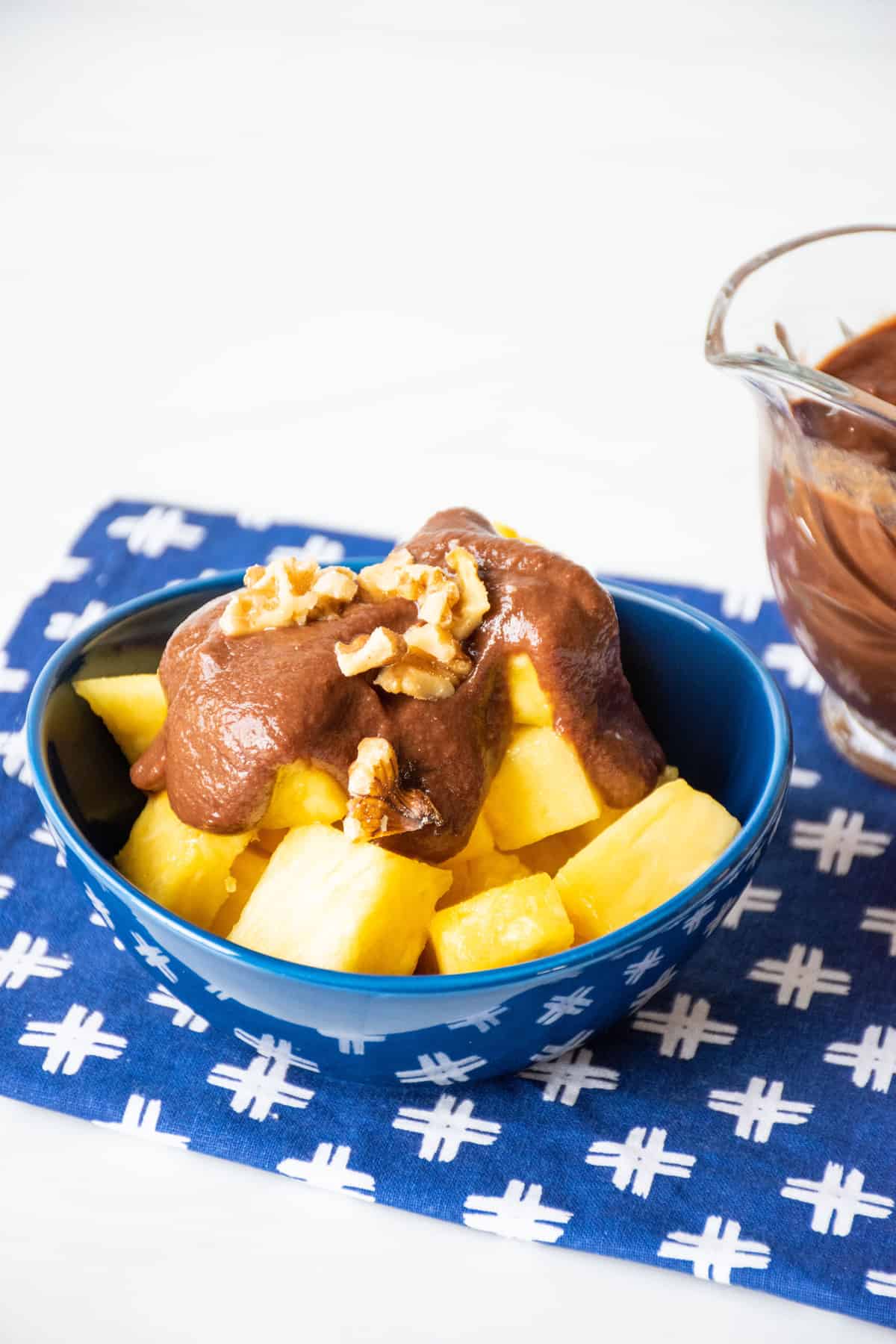 Bowl of pineapple covered with chocolate sauce and chopped walnuts.