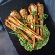 Roasted, halved parsnips, on a platter, with pesto sauce smeared under them.