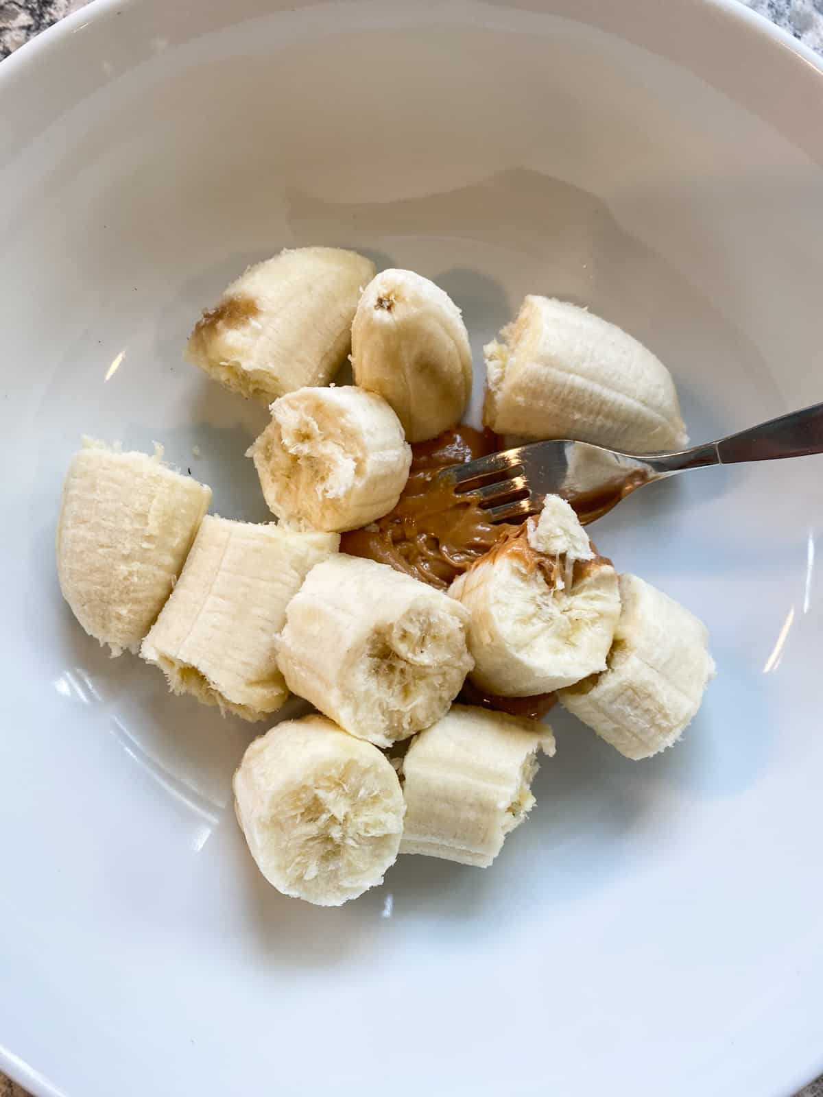 Peeled, broken bananas in a bowl with peanut butter.