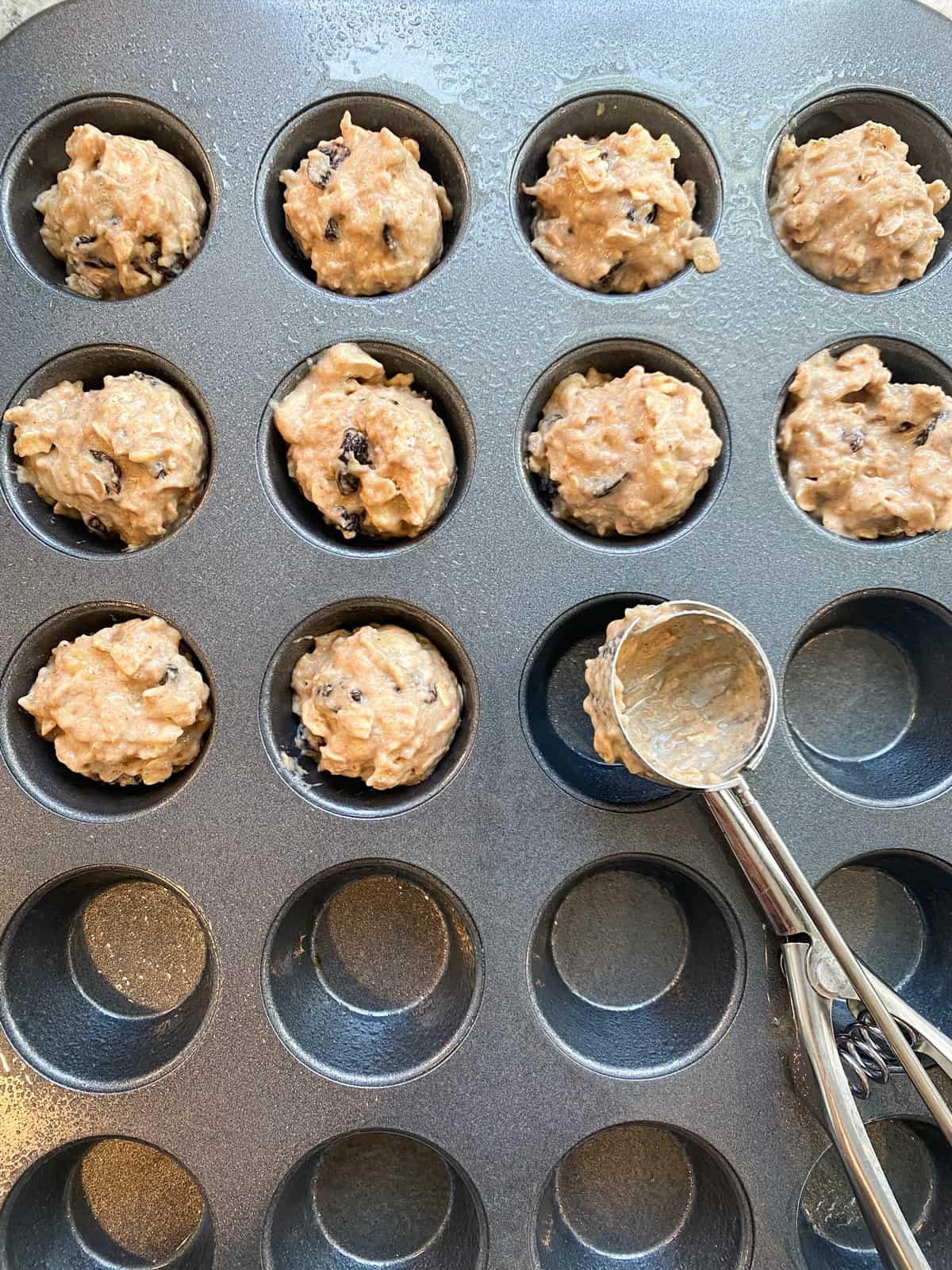 Muffin batter added to half the muffin tin, with scoop visible.