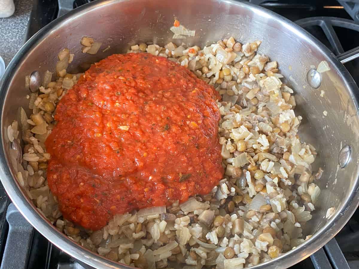 Marinara sauce poured into a pan with cooked filling for stuffed peppers.