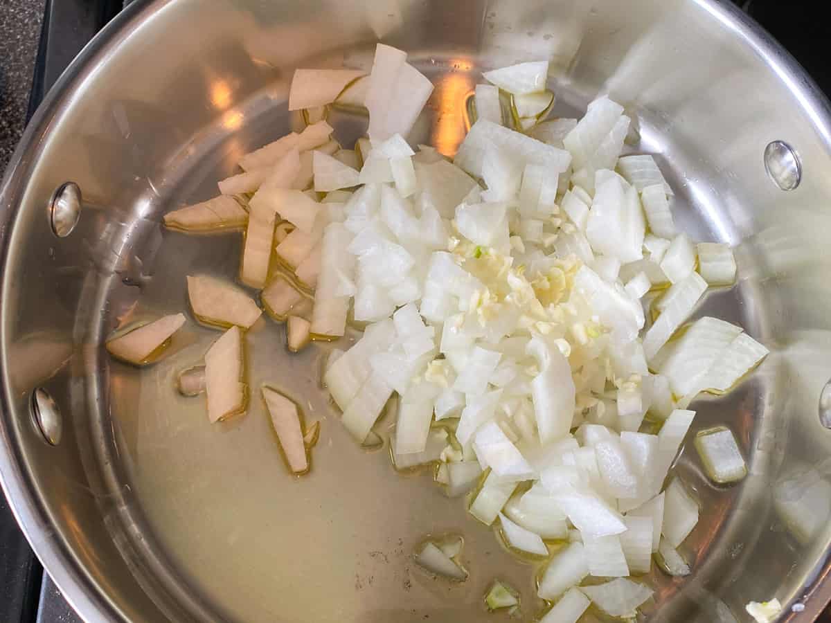 Raw onions and garlic added to a pan with hot oil.