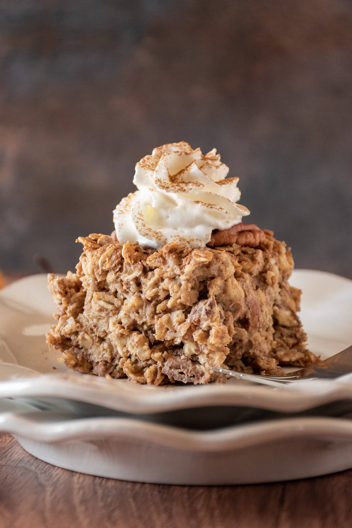 Square of baked oatmeal on a plate, topped with whipped cream and a dusting of cinnamon.