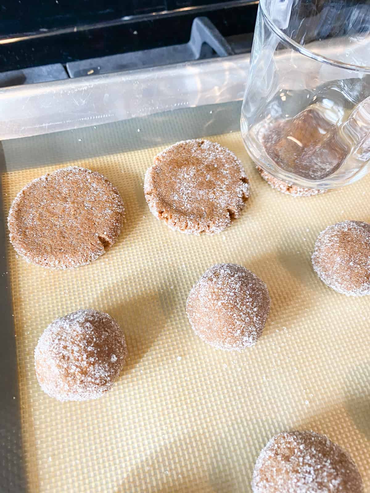 Cookie dough, rolled into balls and sugar; 2 balls are flattened into disks, with a small glass visible, which was used to flatten the cookies.
