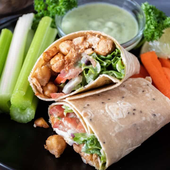 Wrap with chickpeas, lettuce, tomato and onion, cut in half, on a plate with celery and carrot sticks.