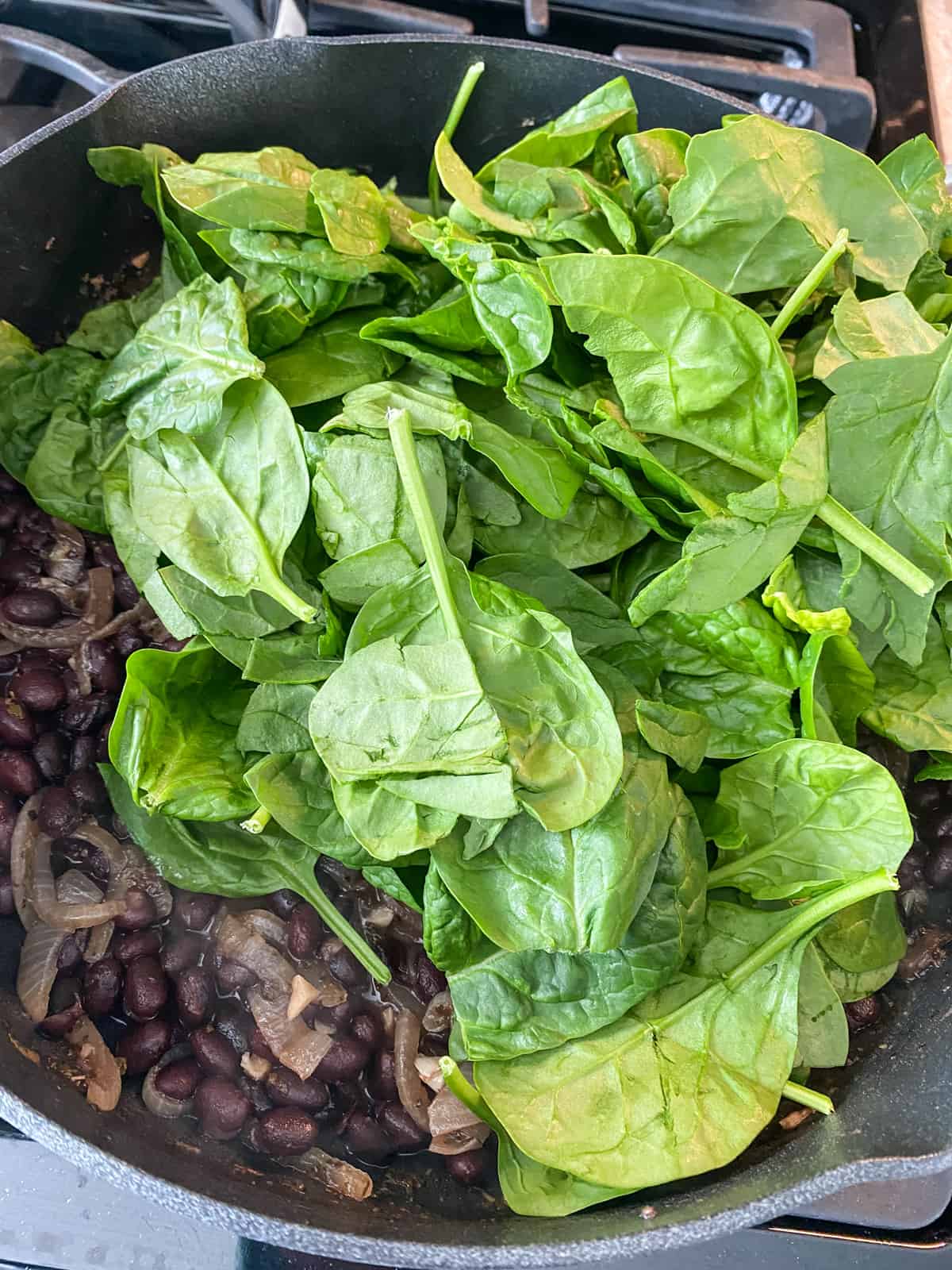 Spinach added to the skillet of black beans.