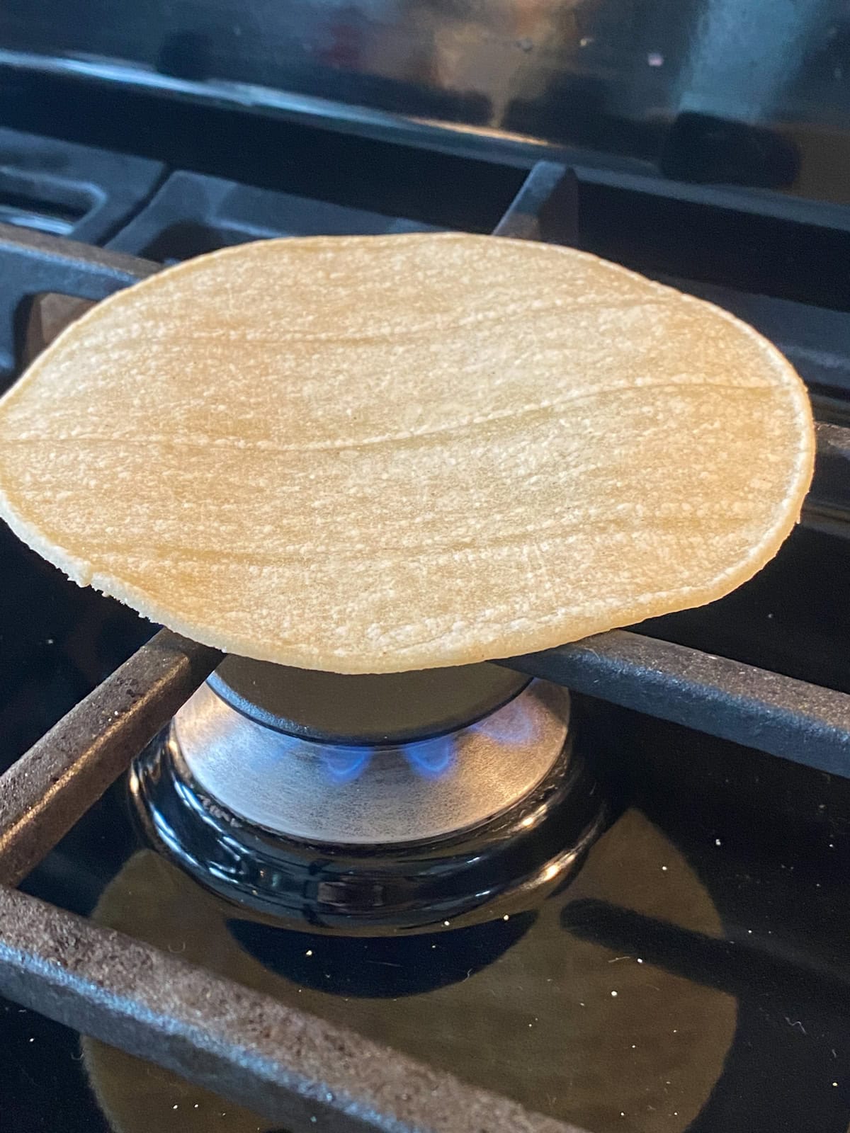 A corn tortilla toasting on a gas stove grate.