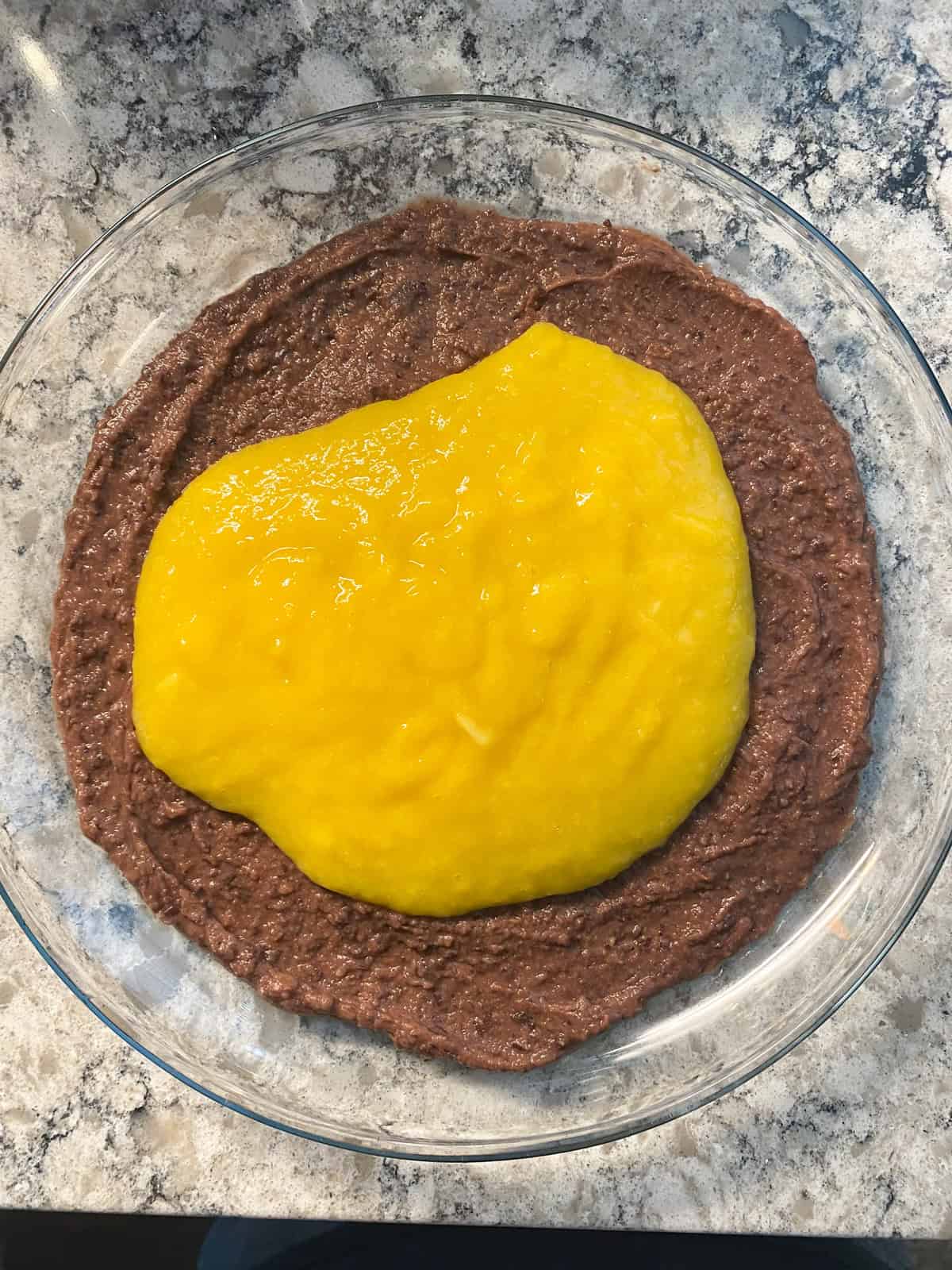 Black bean dip spread on a plate, with mango puree poured over.
