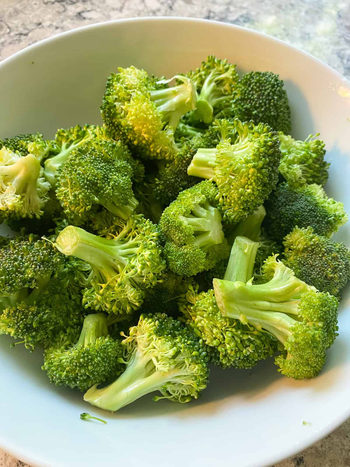 Raw broccoli florets, in a bowl, tossed with olive oil, garlic, and lemon juice.