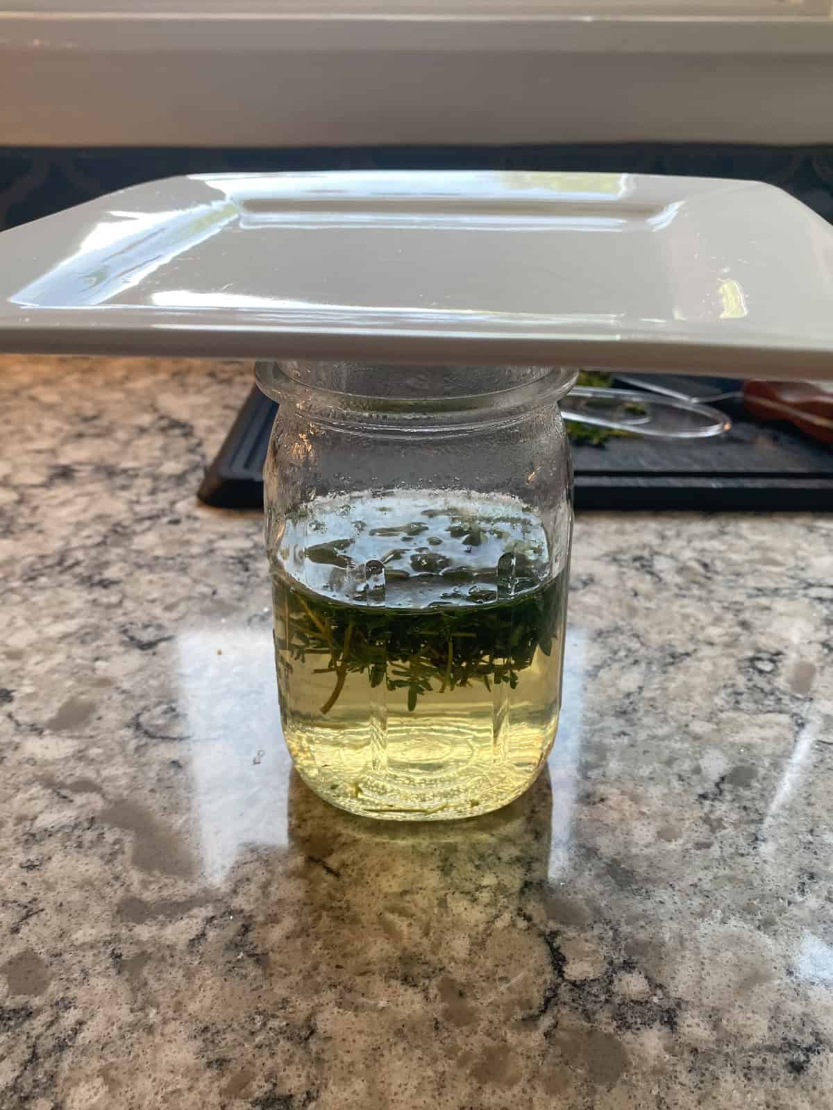 Jar with chopped thyme and hot water, with a plate cover the top, steeping.