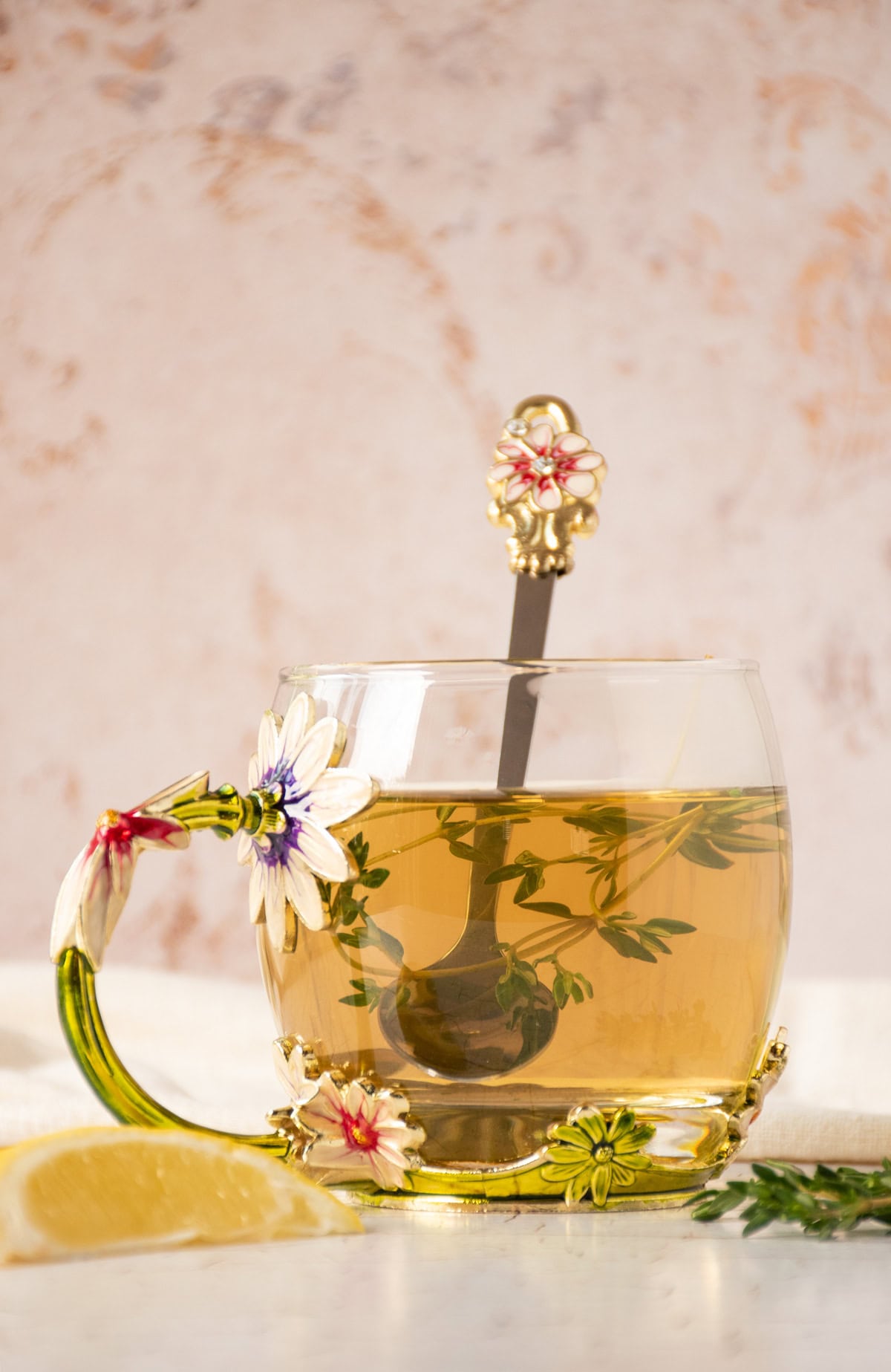 Tea in a glass mug, with thyme sprigs and a spoon in it.