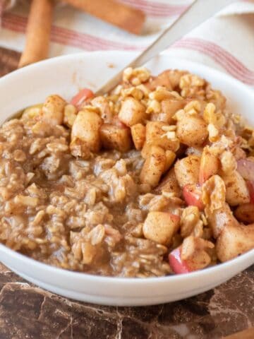 Bowl of oatmeal with sauteed apples and walnuts on top.