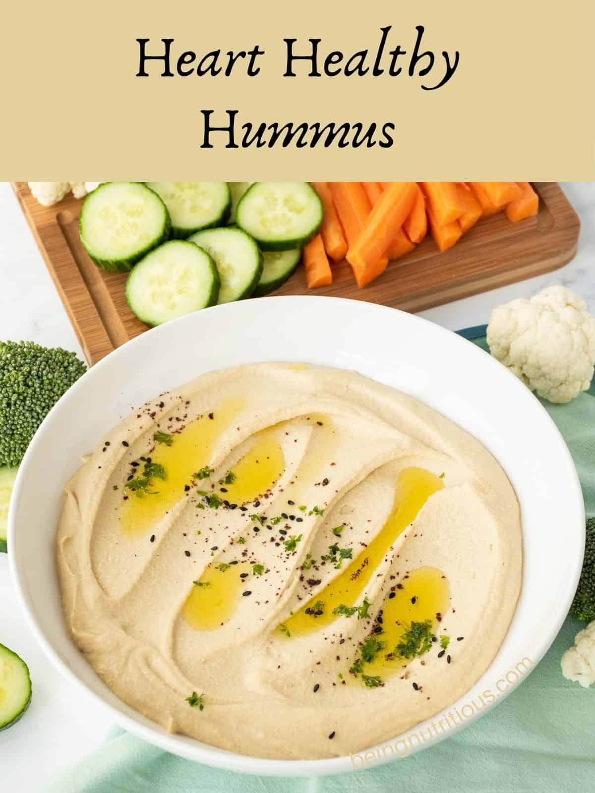 Bowl of creamy hummus, garnished with an olive oil drizzle, and a sprinkle of parsley, black sesame seeds, and sumac. Text overlay: Heart Healthy Hummus.