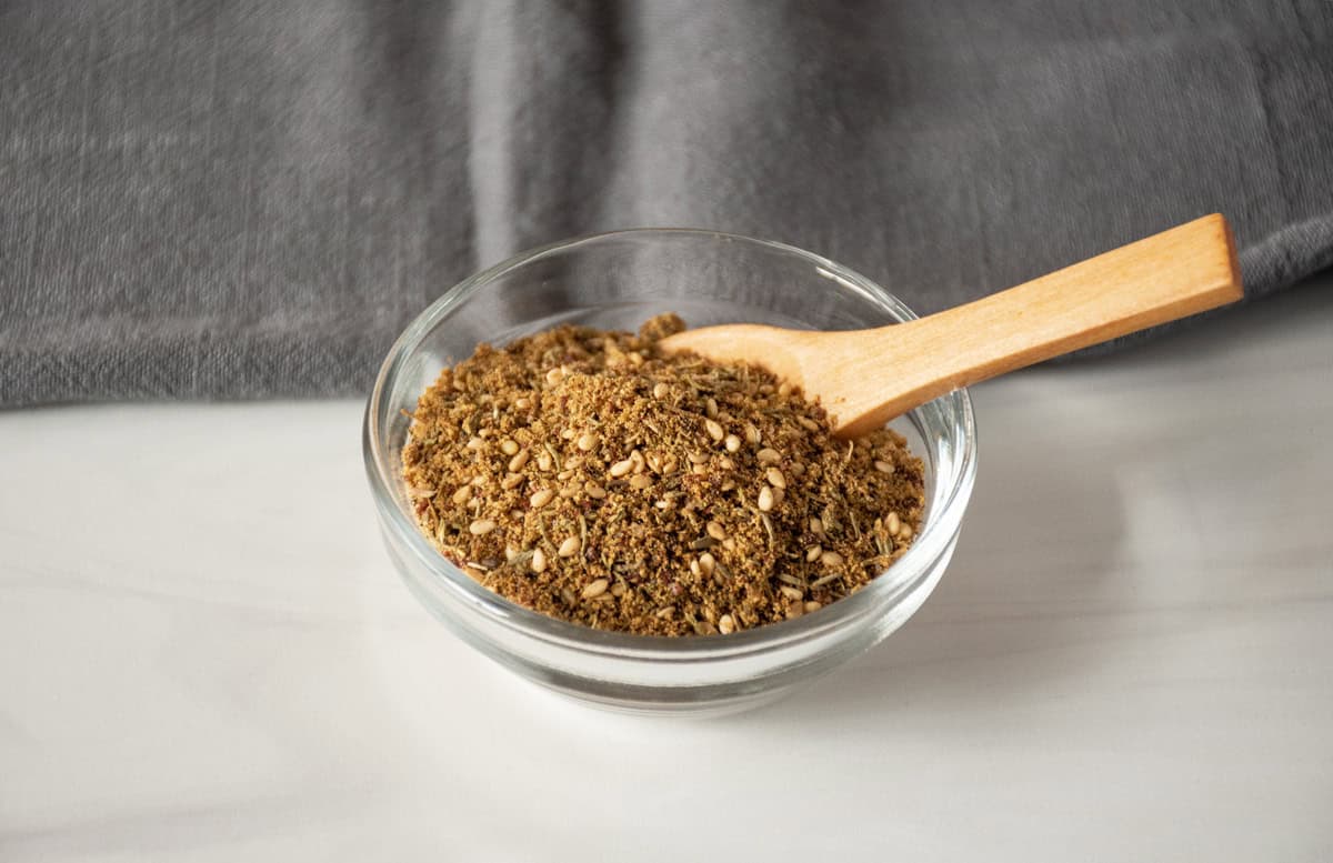 Small glass bowl with spice blend in it and a small wooden spoon.