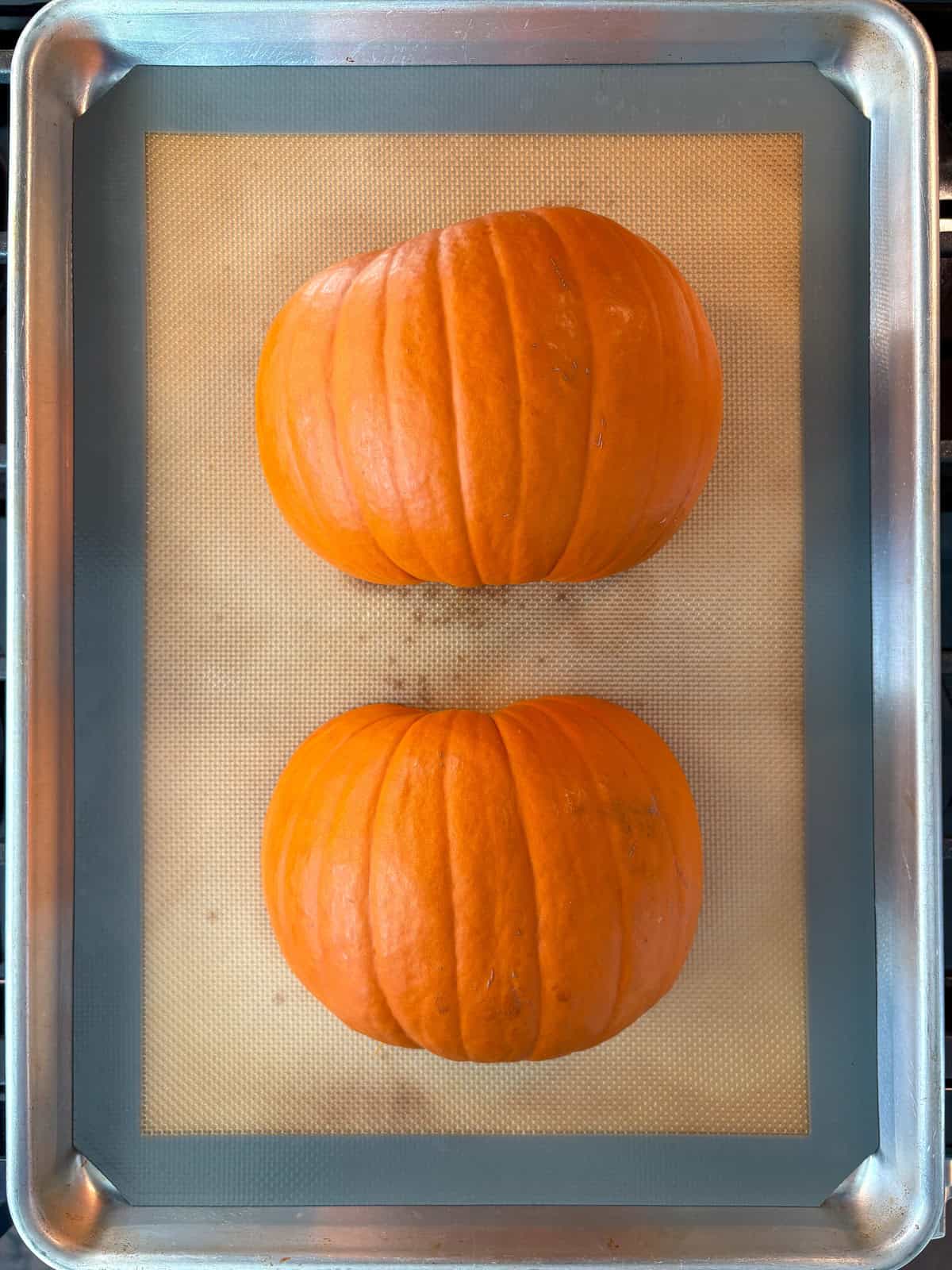 Raw pumpkin halves, face down on a baking sheet.