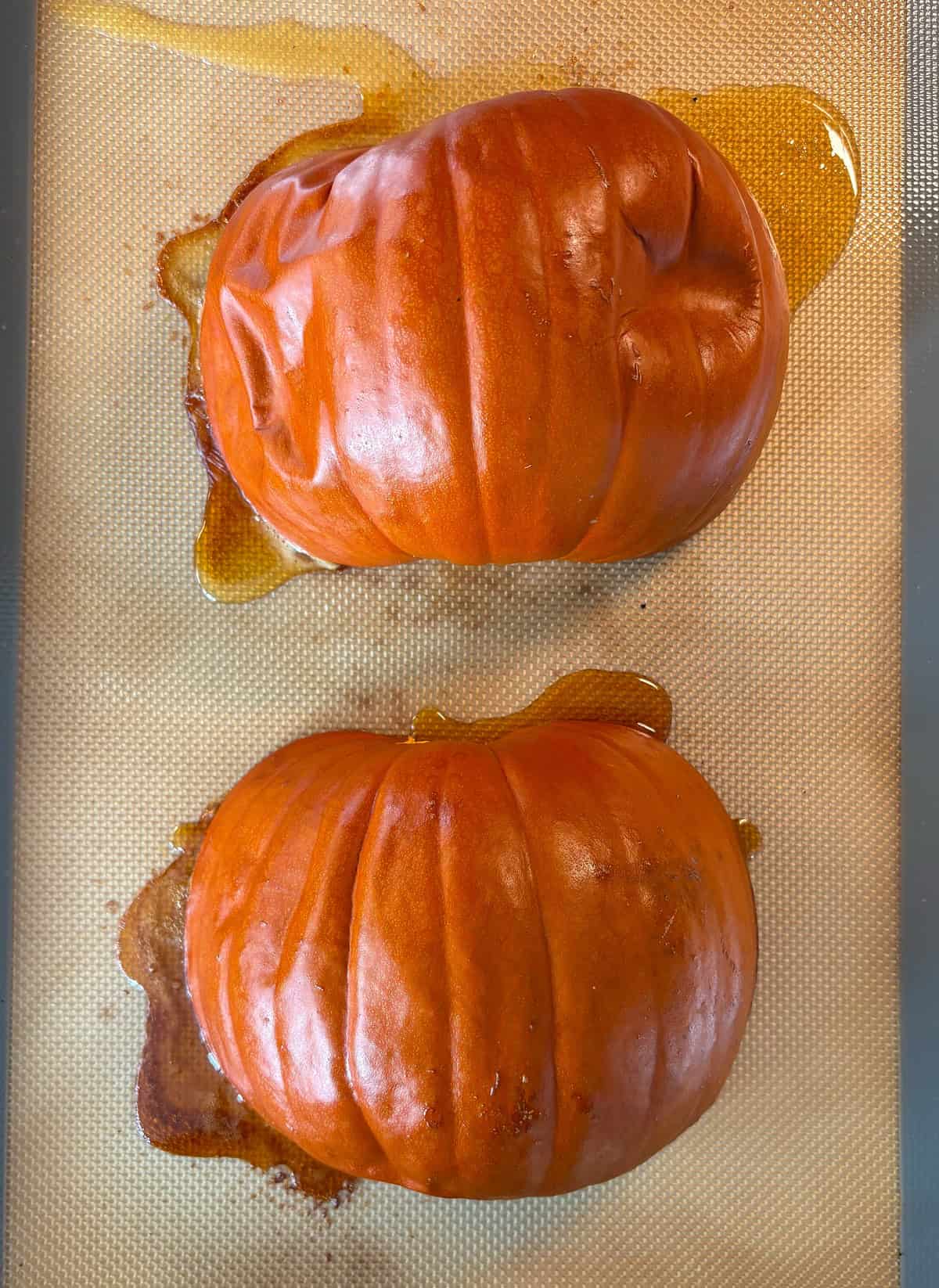 Baked pumpkin halves, face down on a baking sheet.