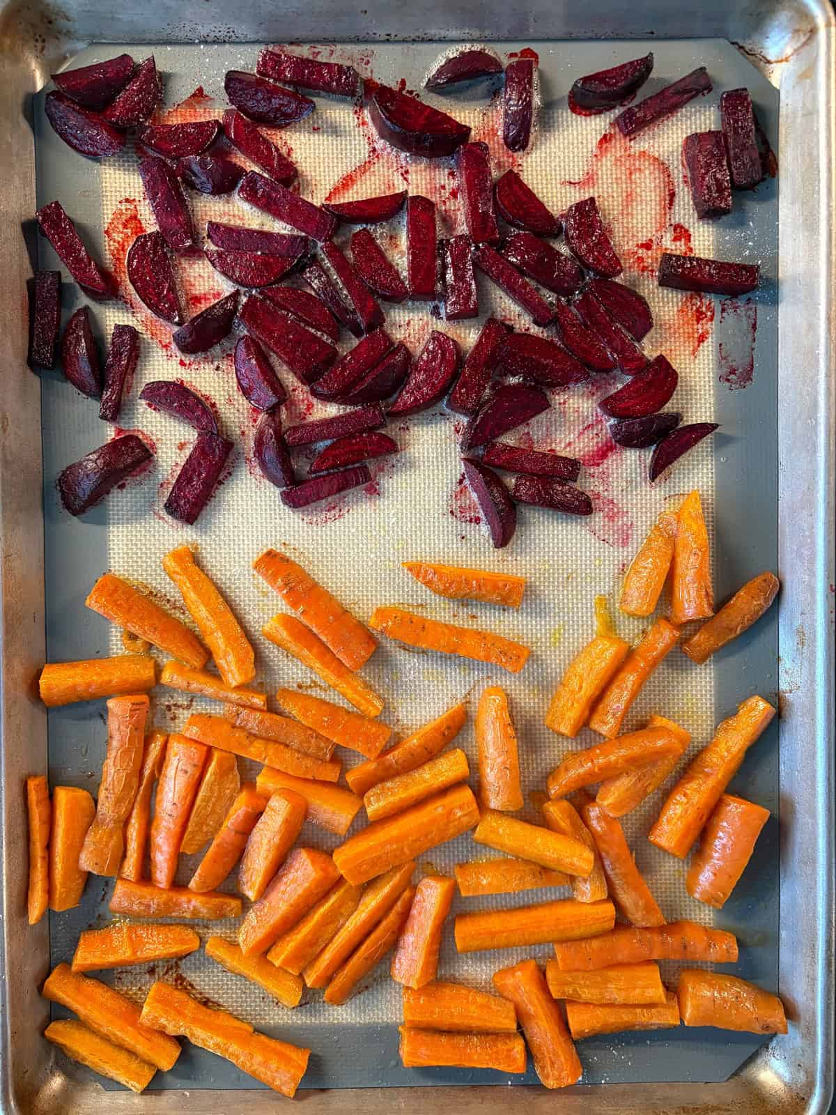 Beets and carrots, roasted, on a baking sheet.