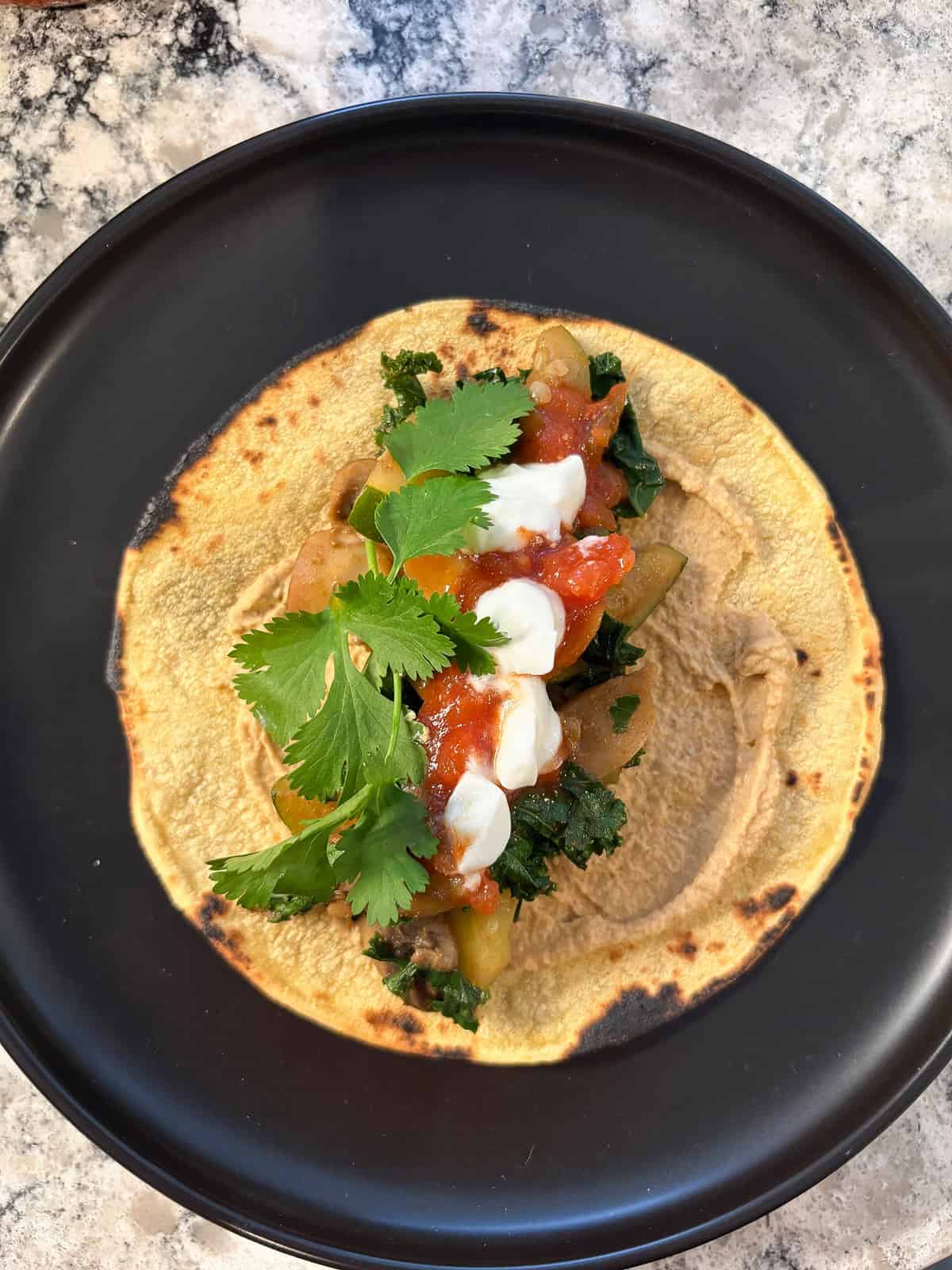 Completed taco, with garnishes of salsa, Greek yogurt, and cilantro added on the filling.