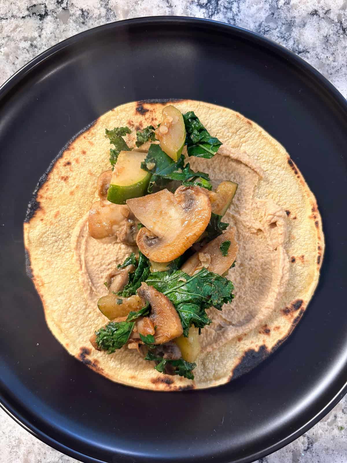 Mushroom, zucchini, and kale filling spooned on top of the hummus smear on the tortilla.