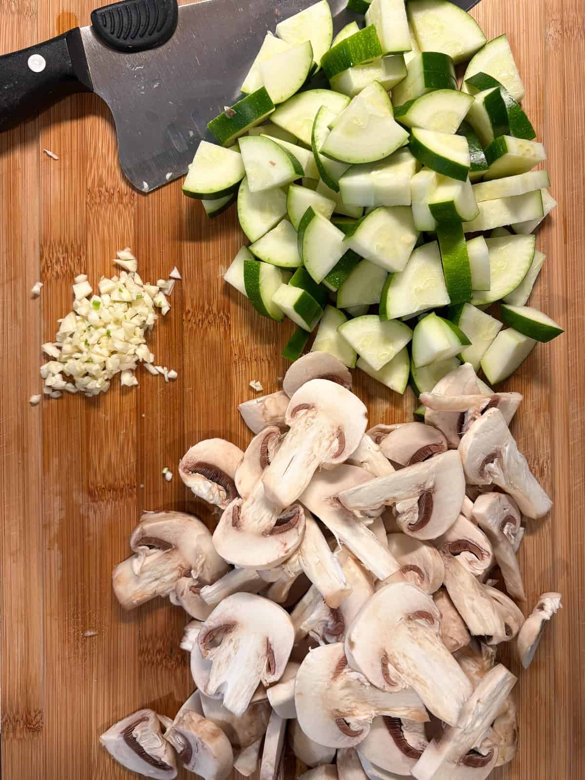 Chopped mushrooms and zucchini, and minced garlic on a cutting board.