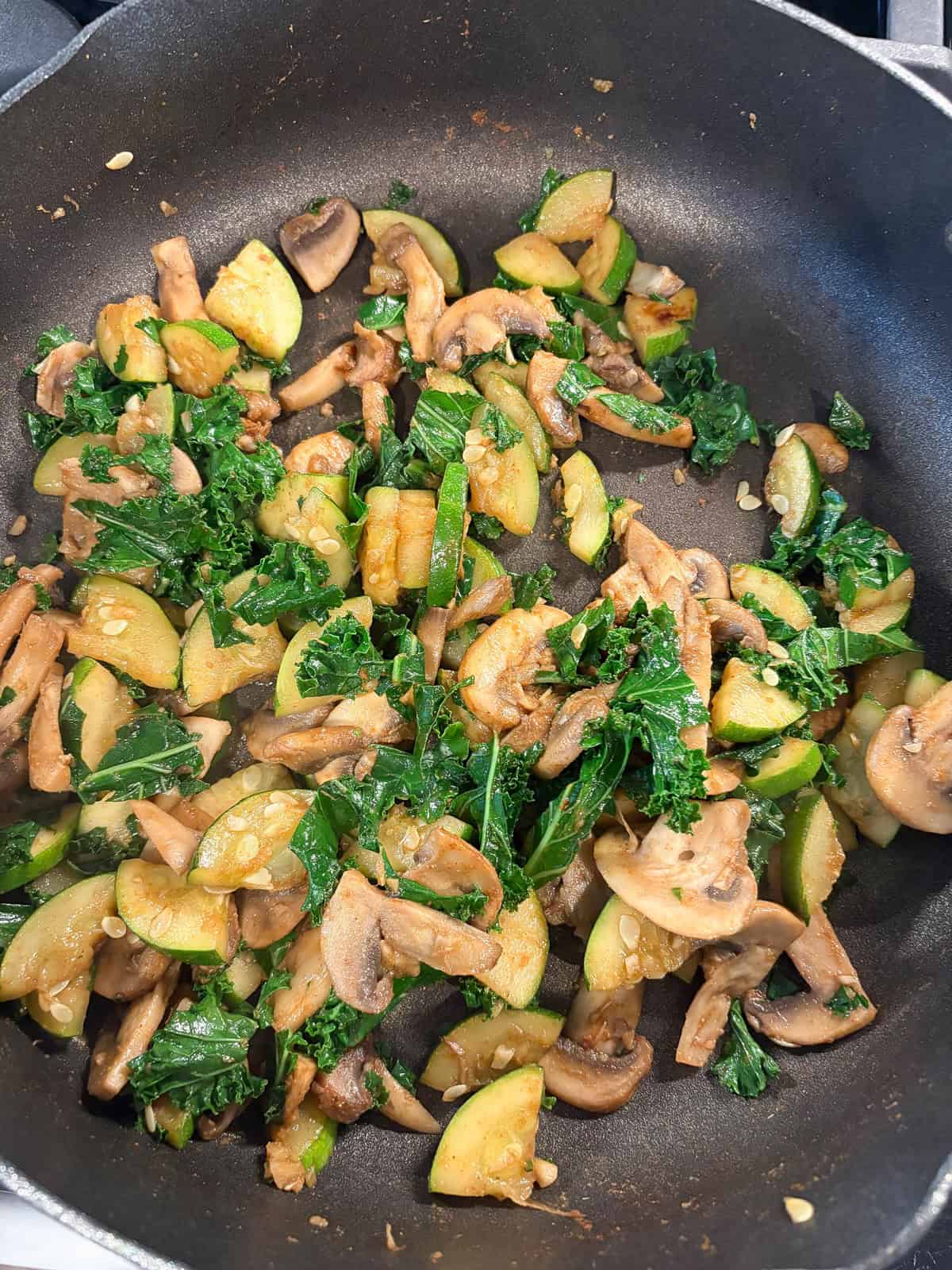 Sauteed mushrooms, zucchini, and kale in a pan.