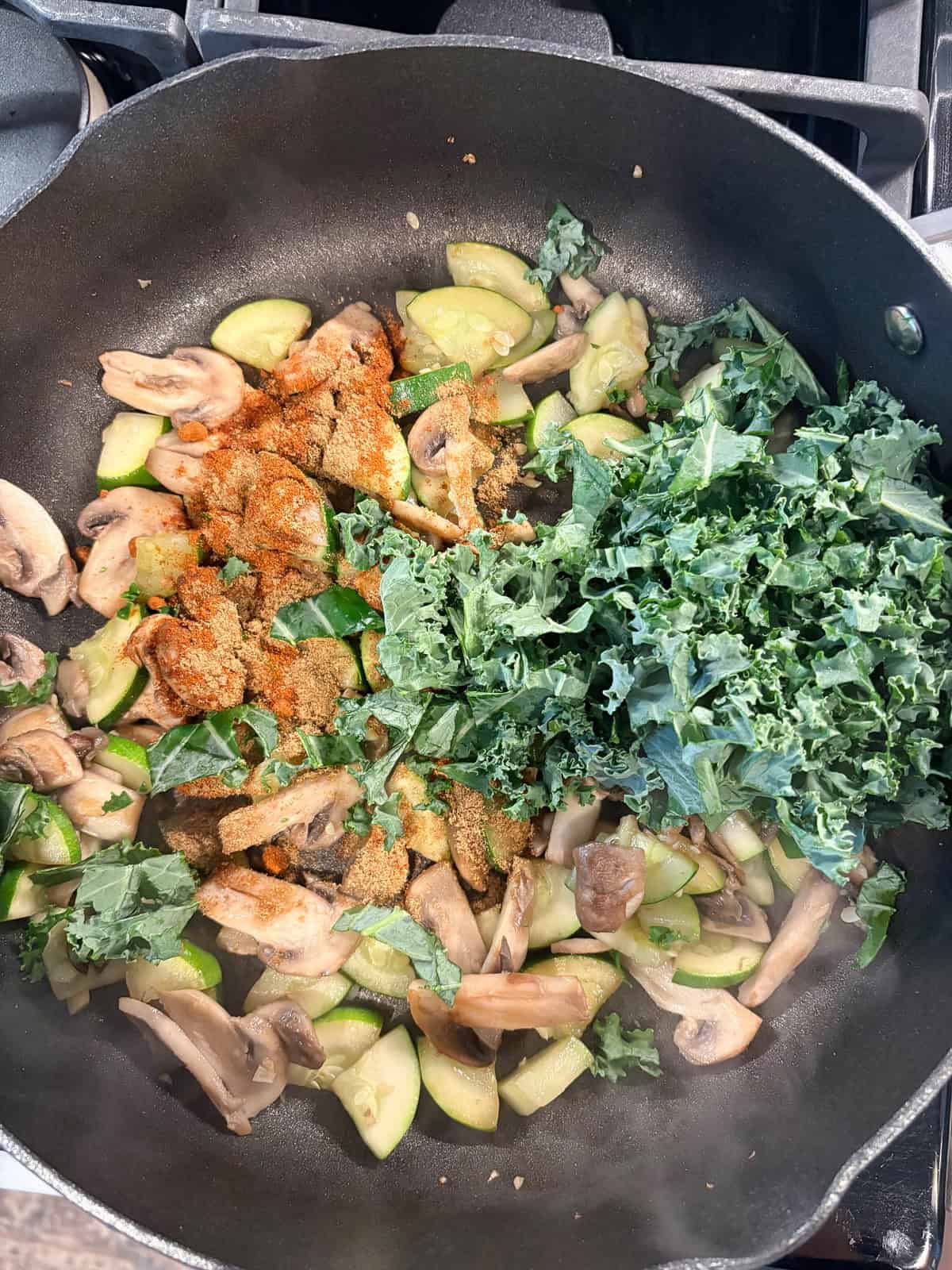 Kale added to the pan of sauteing vegetables.