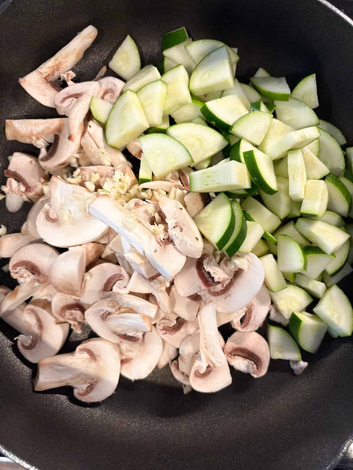 Chopped mushrooms and zucchini sautéing in a pan with oil and garlic.