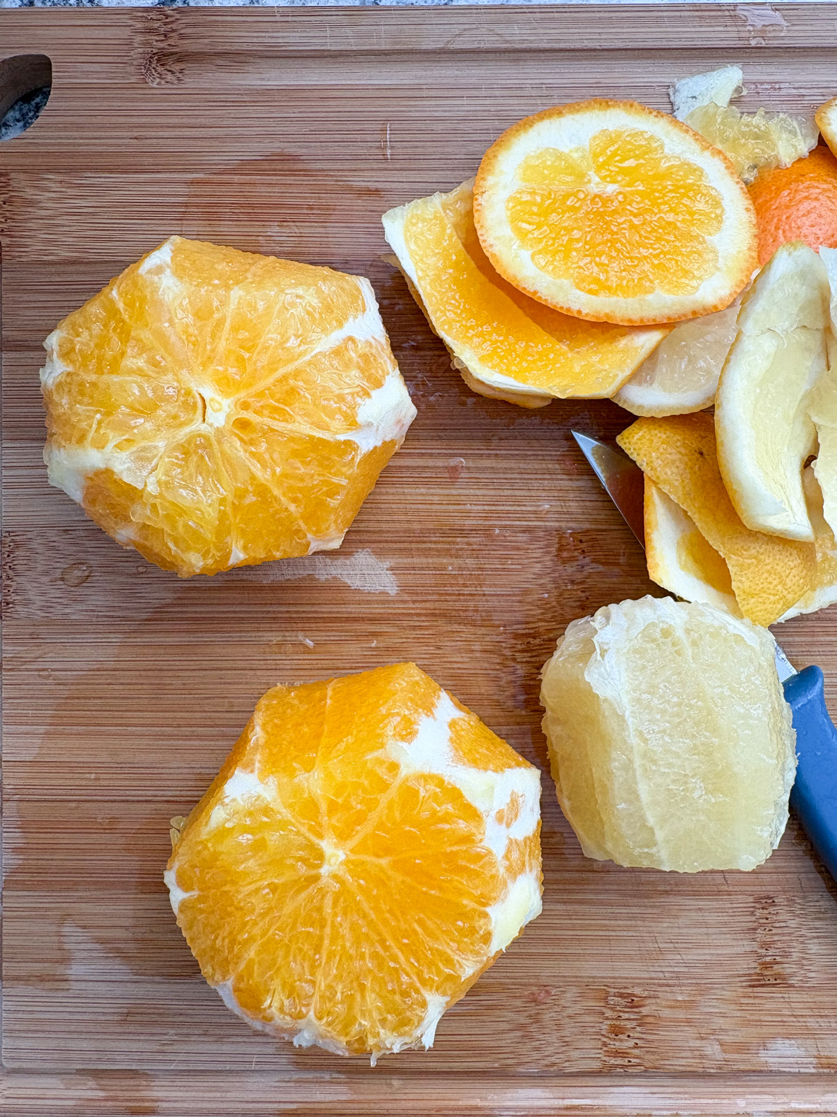 Two oranges and a lemon with their peels cut off, on a cutting board.