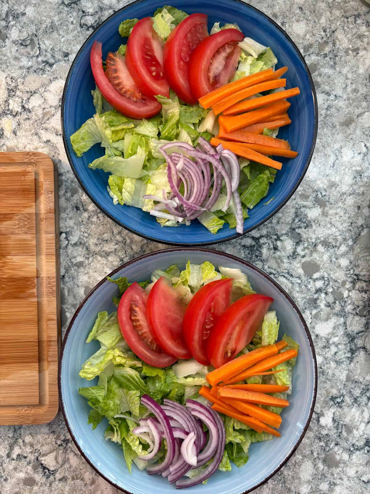 Tomatoes, carrots, and onions arranged on the lettuce, in the salad bowls.