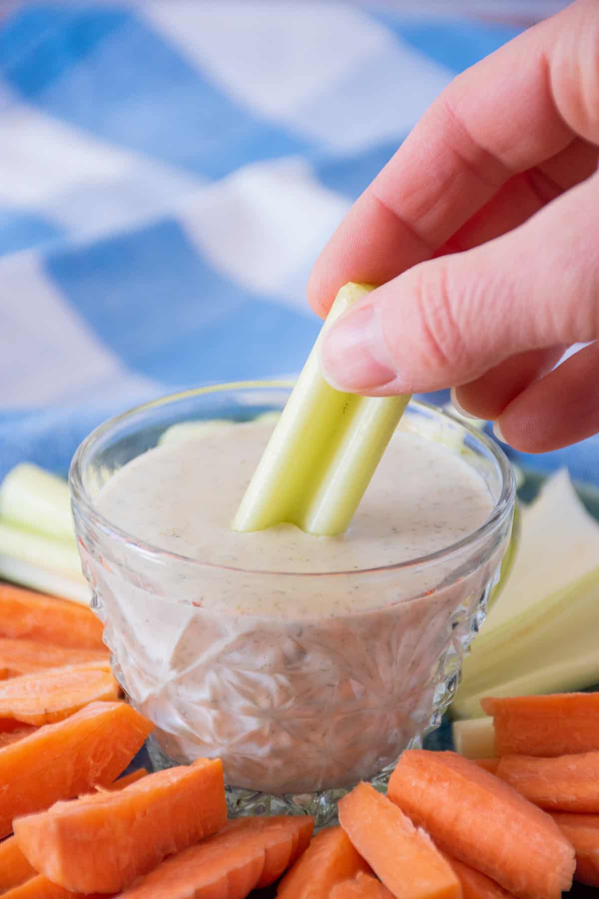 Small plate with carrot and celery sticks on it, and a small bowl of ranch dressing in the middle. A hand is dipping a celery stick into the dressing.